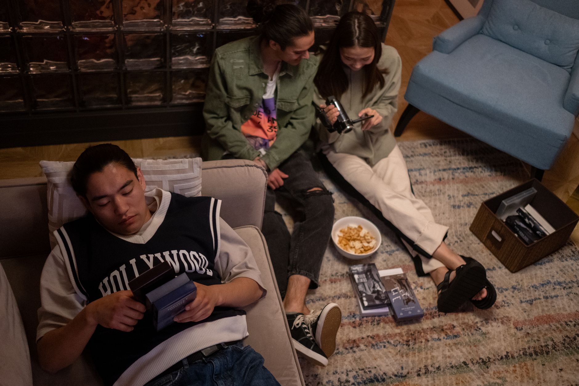 Teenagers relax indoors for a nostalgic movie night with chips and VHS tapes.