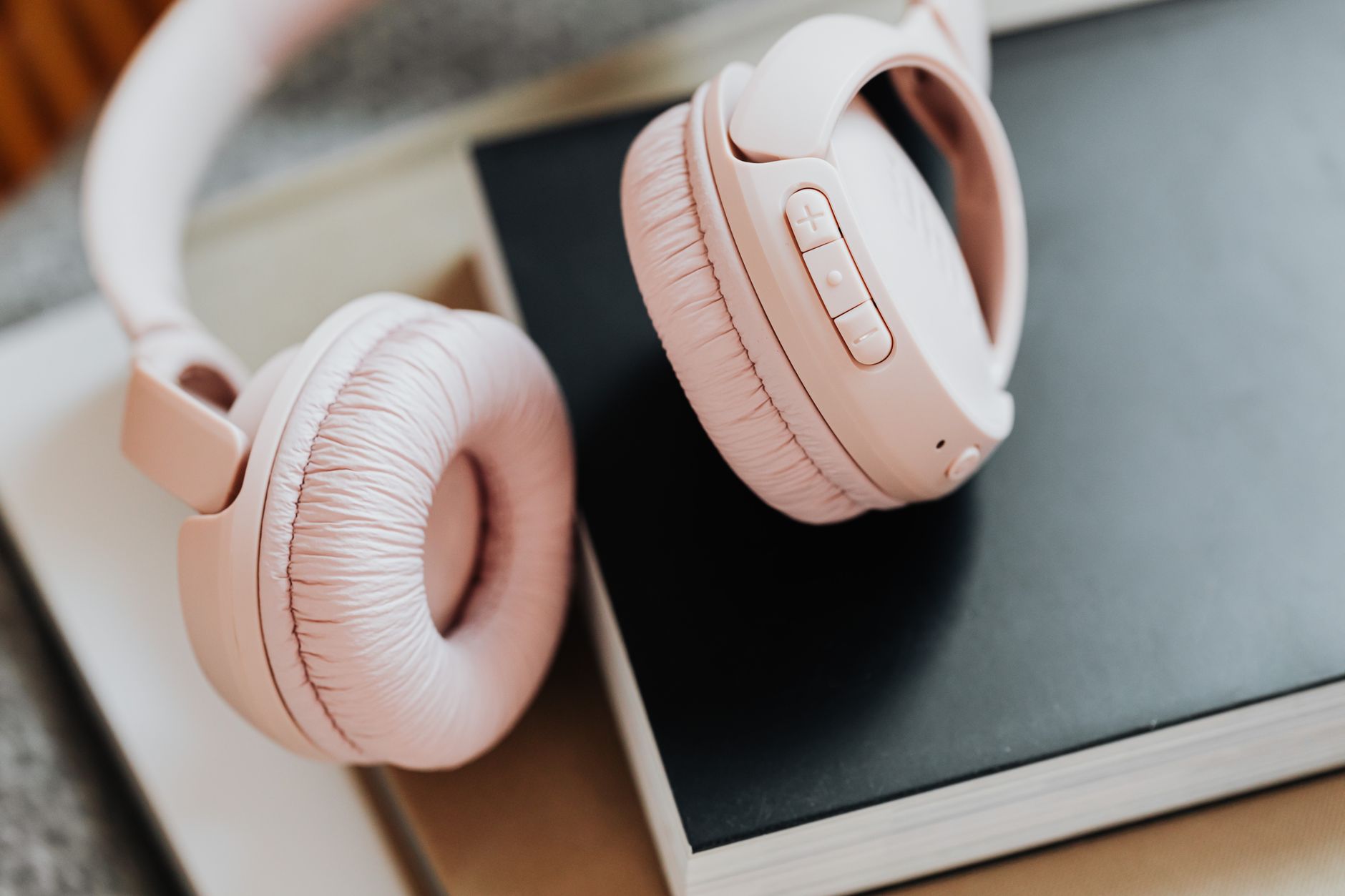 Soft pink wireless headphones placed on stacked books, ideal for music enthusiasts.