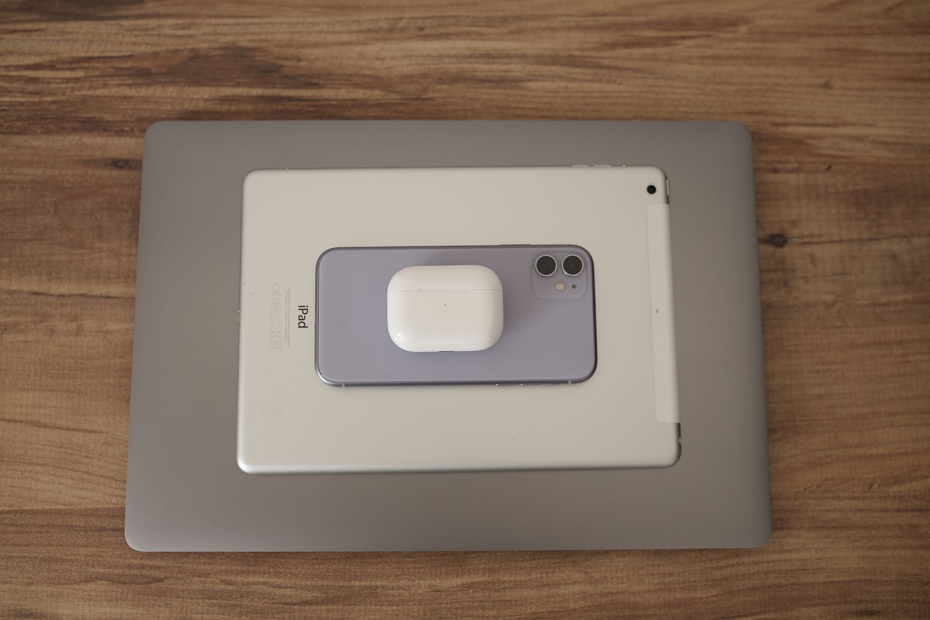 Flat lay of modern technology devices including smartphone, tablet, and earbuds on wooden surface.