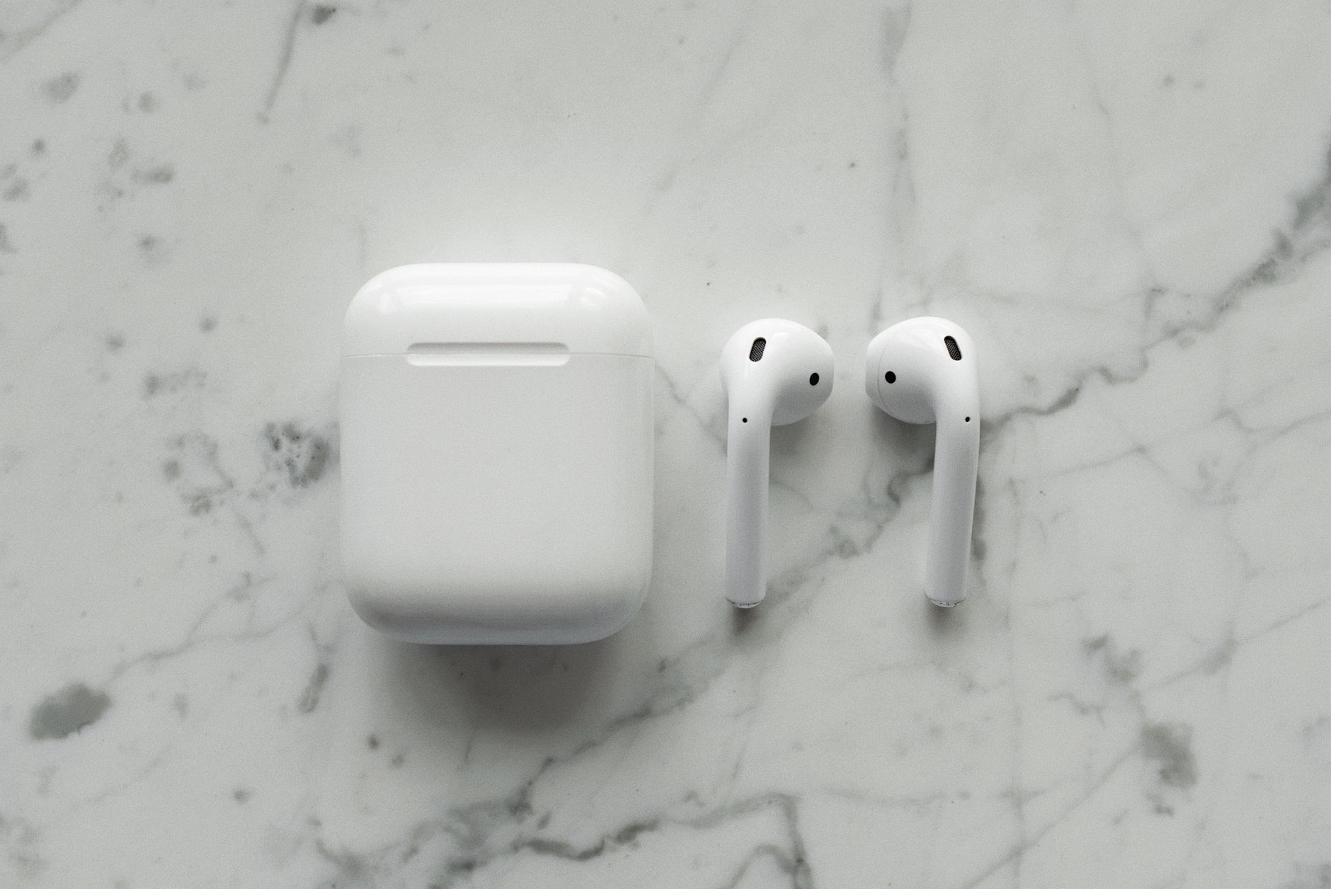 Close-up of modern wireless earbuds and case on a sleek marble surface, showcasing minimalist technology.