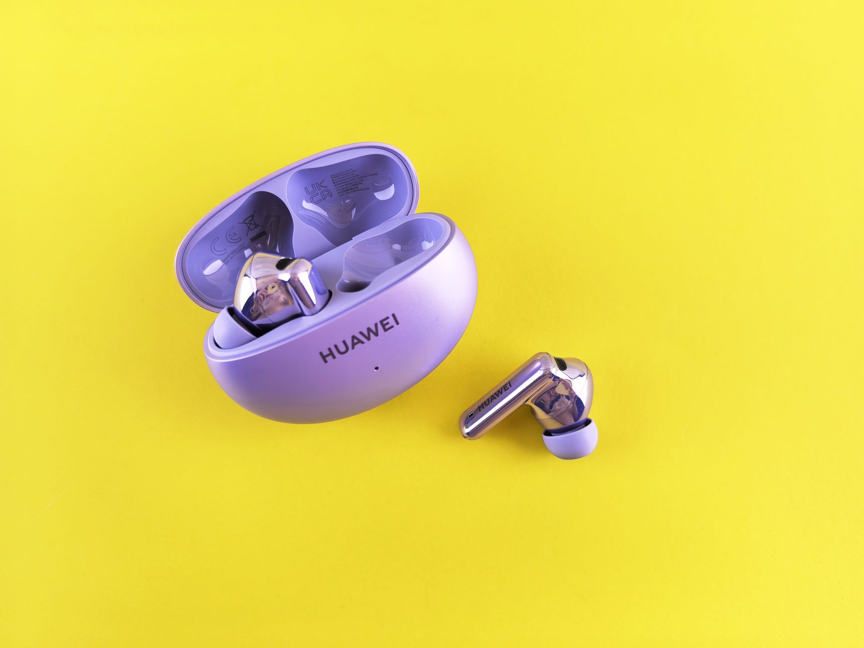 Close-up of sleek wireless earbuds and case on a vibrant yellow background.