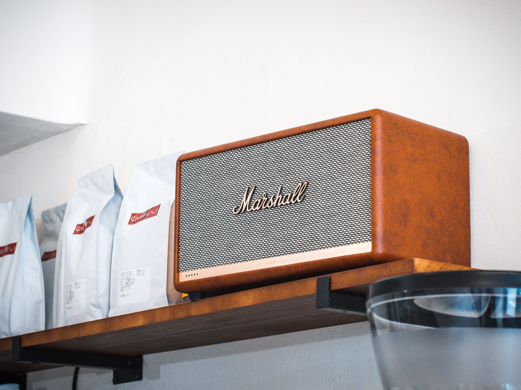 Stylish Marshall speaker showcased on a wooden shelf inside a modern café environment.