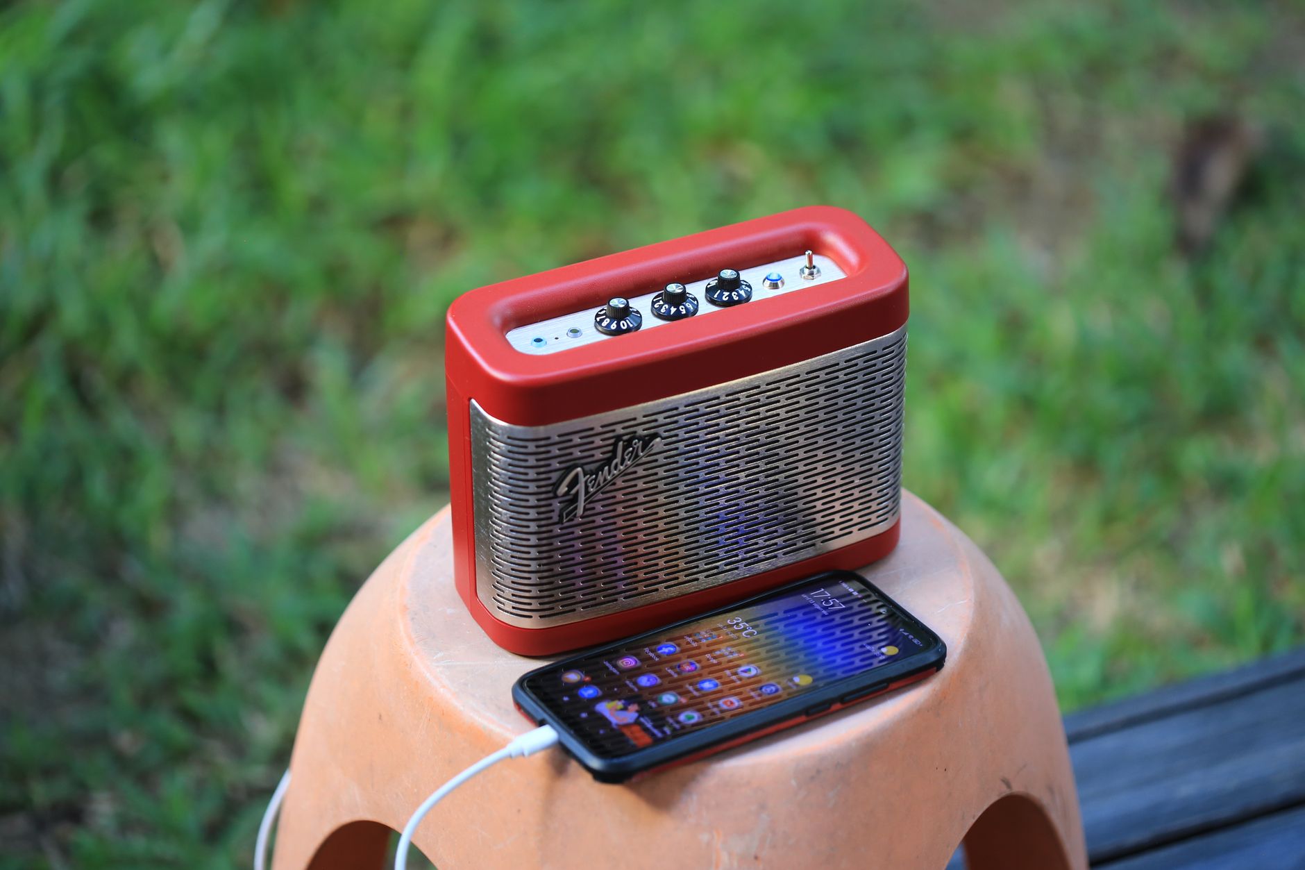 Red portable speaker and smartphone on a stool outdoors, showcasing modern gadgets in nature.