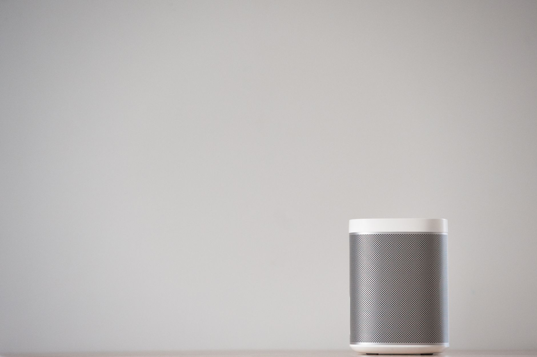 A sleek, wireless smart speaker on a wooden table against a plain wall.