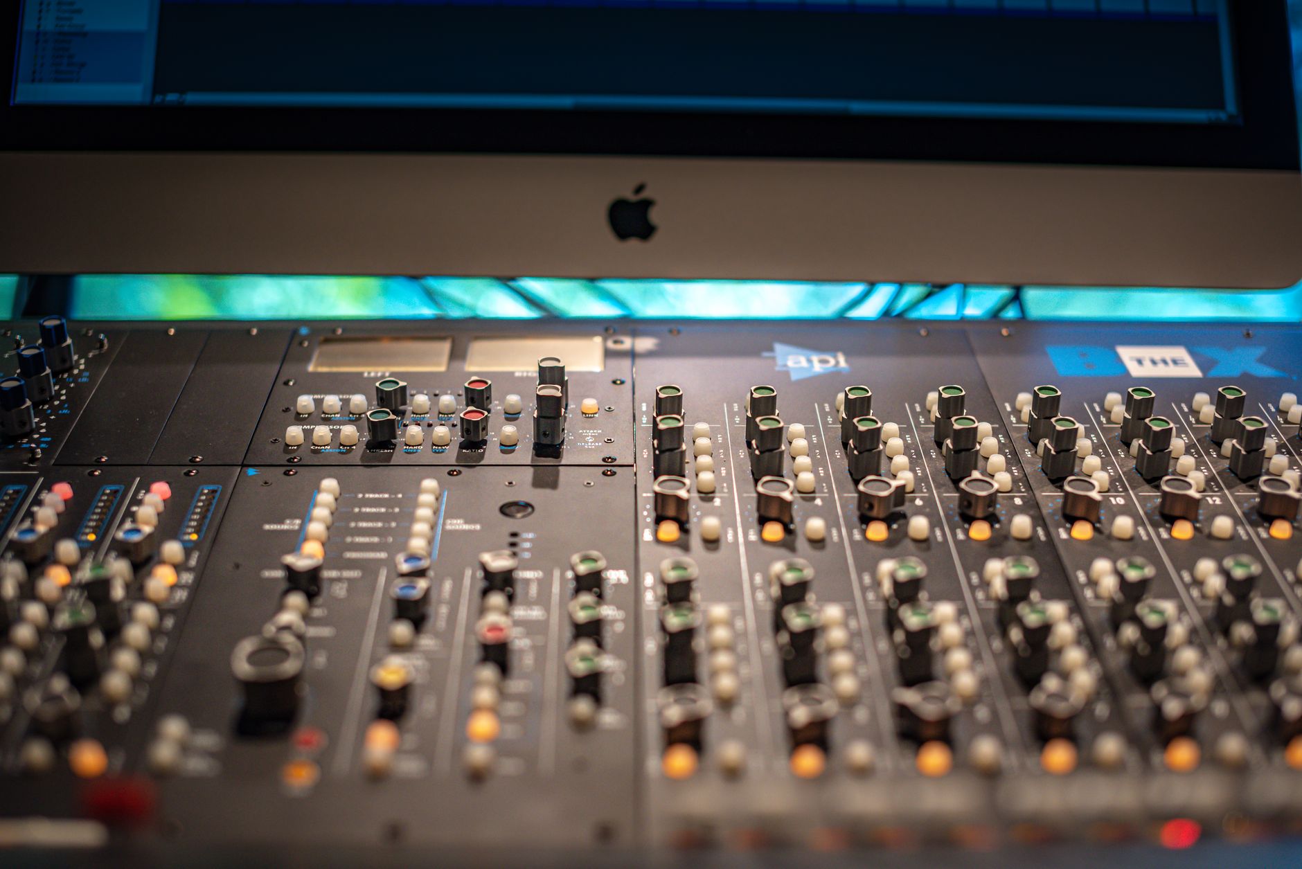 Close-up view of a professional audio mixing console in a modern recording studio with Apple equipment.
