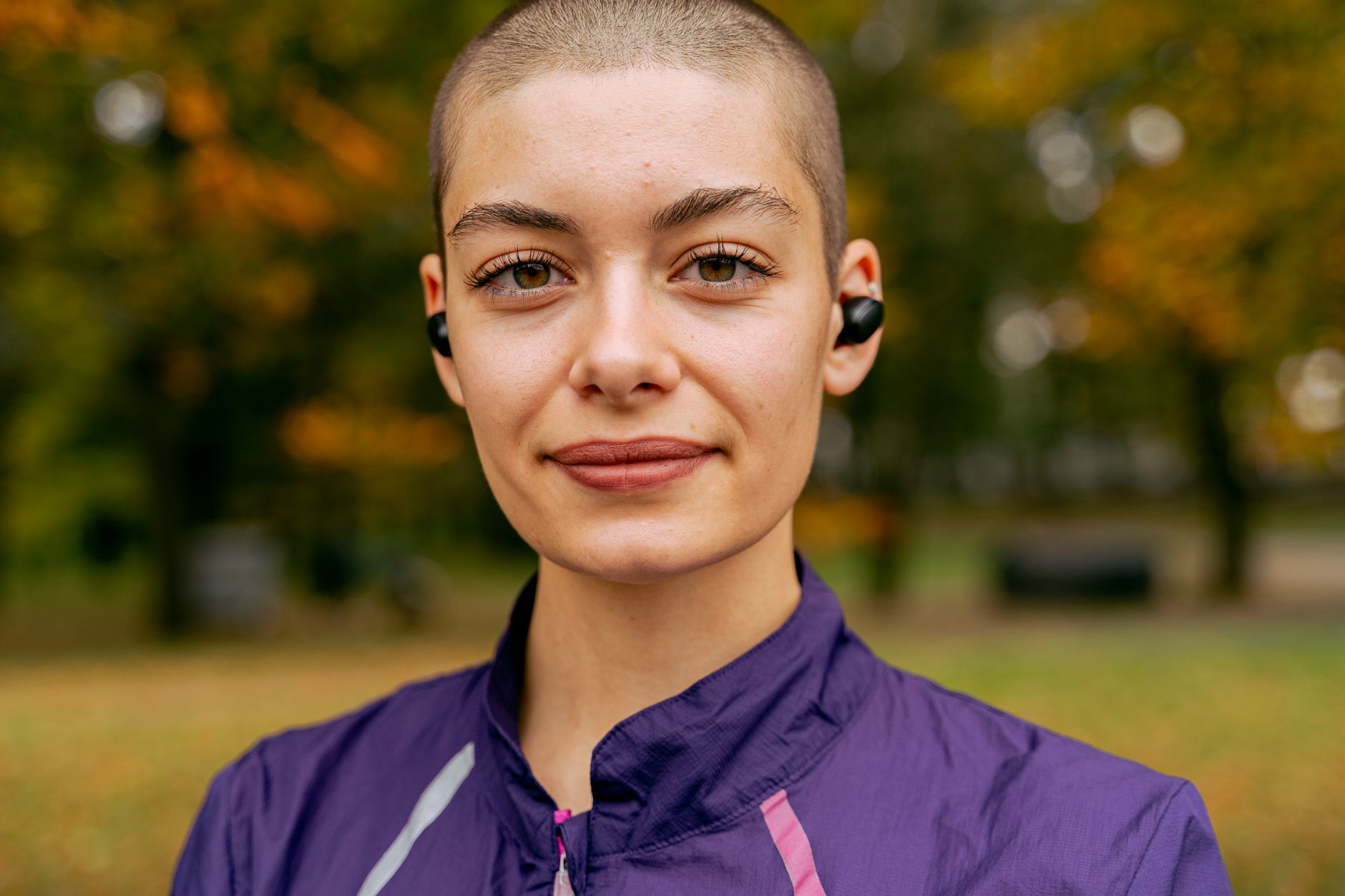 Close-up of a confident woman in a park, wearing earbuds in autumn.