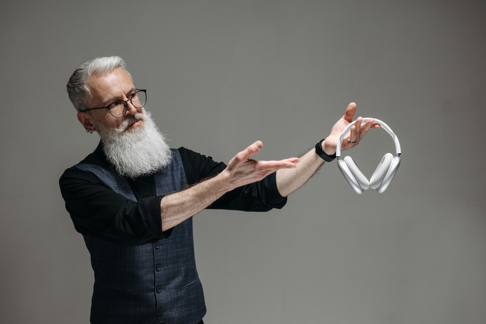 Bearded man with eyeglasses showcasing modern wireless headphones against a gray background.