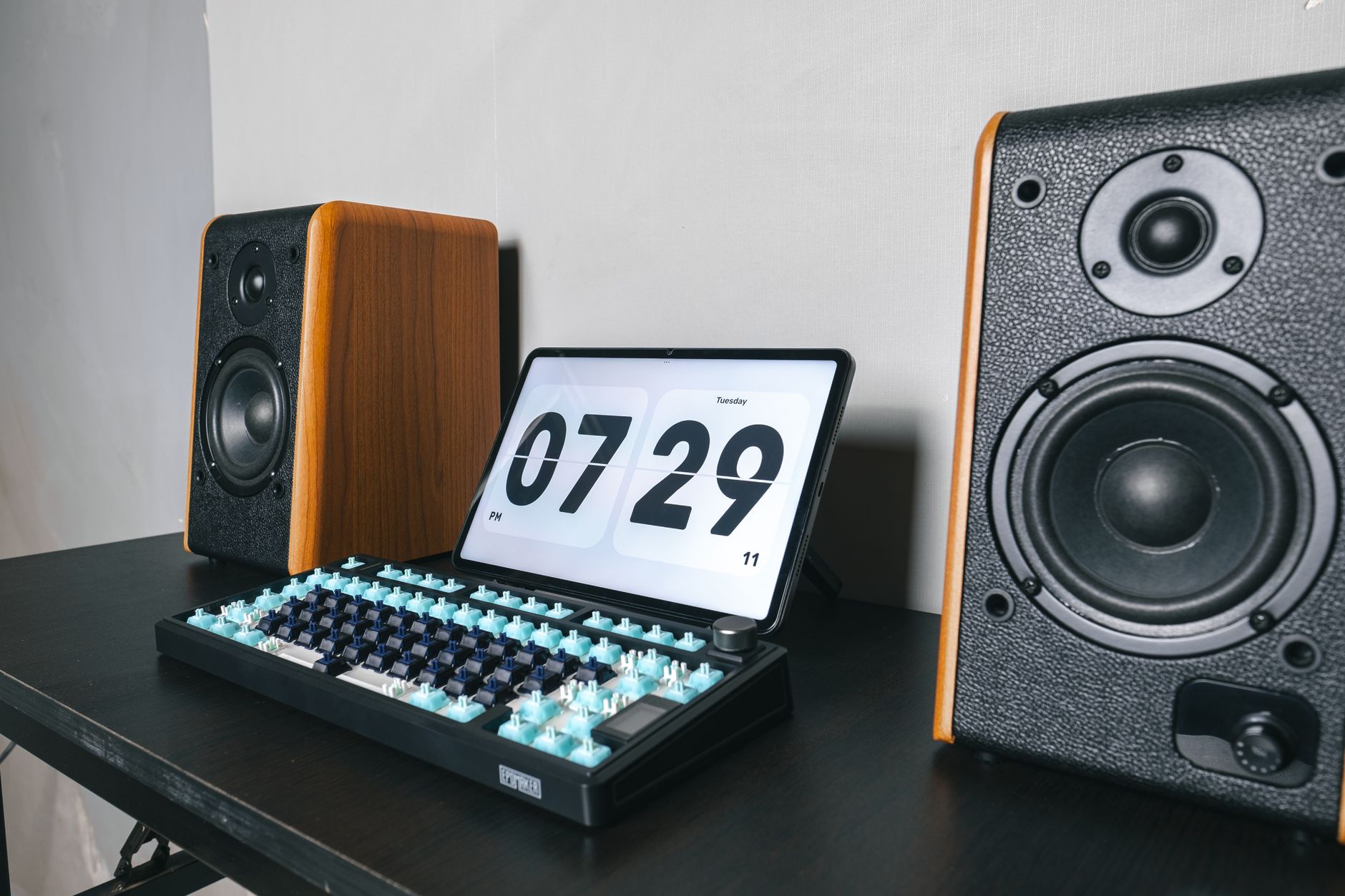 A sleek home office setup featuring a mechanical keyboard, digital clock, and speakers.