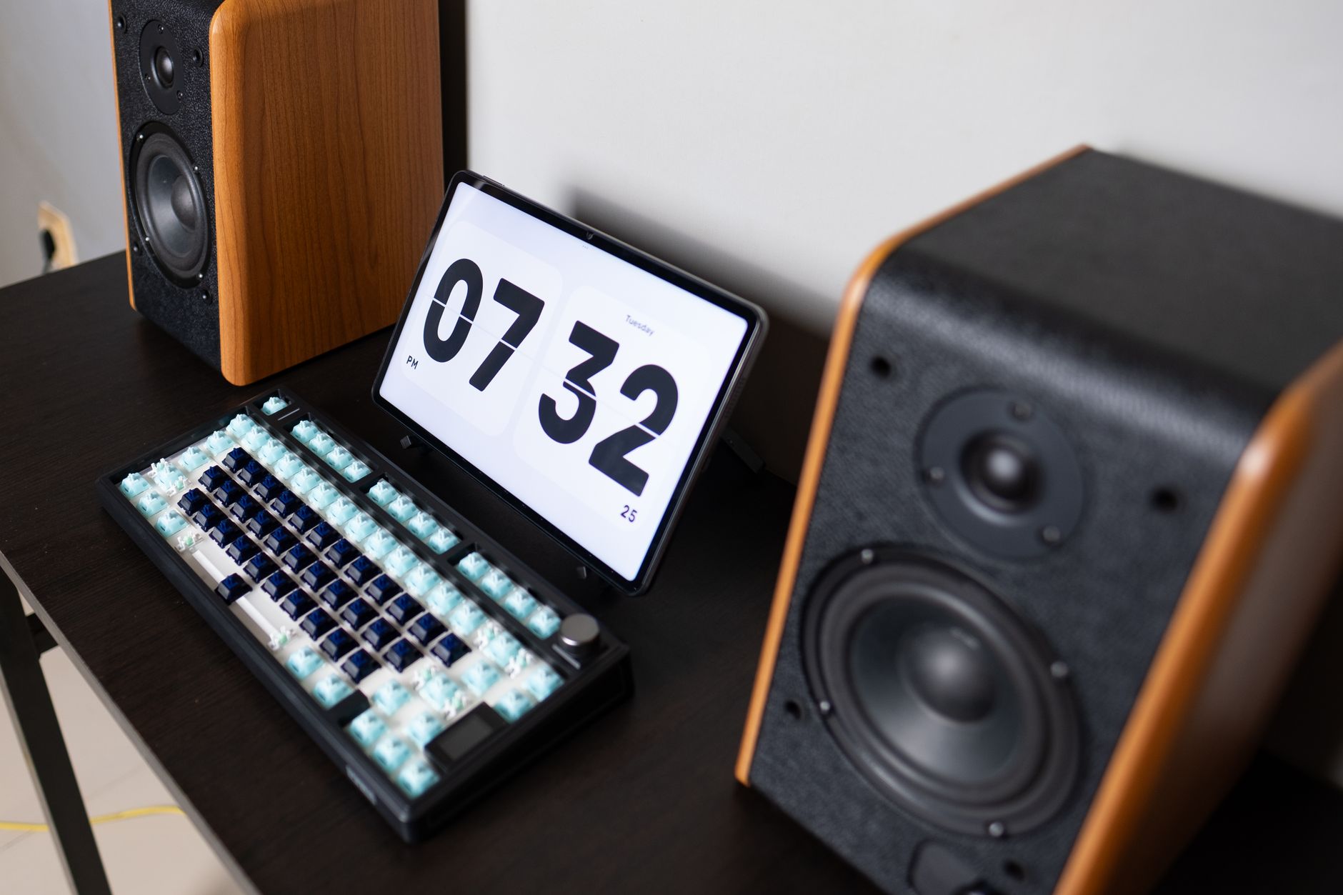 Modern desktop setup featuring speakers, a mechanical keyboard, and a digital tablet displaying the time.