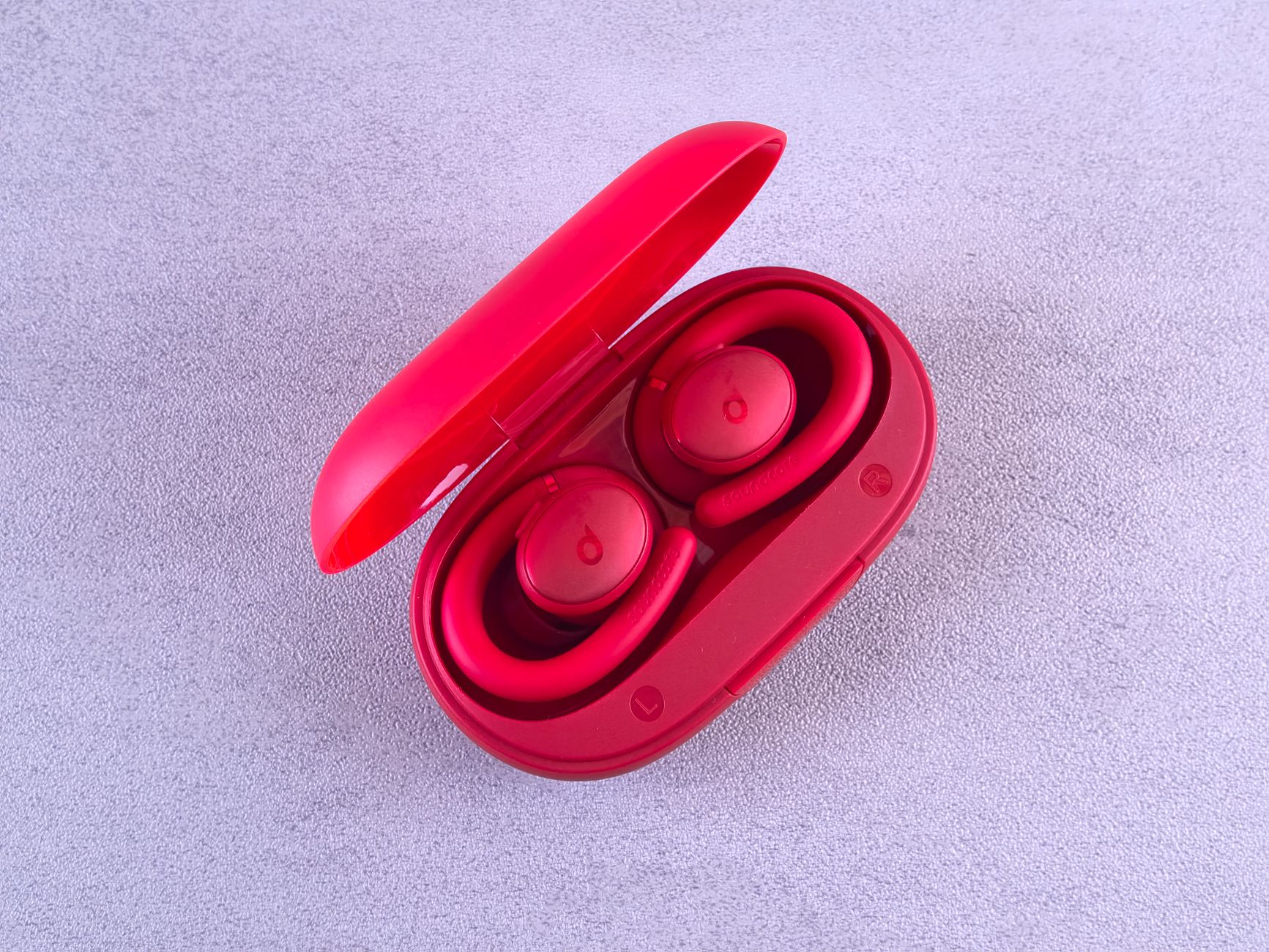 Top-down view of vibrant red wireless earbuds in an open charging case on a textured surface.