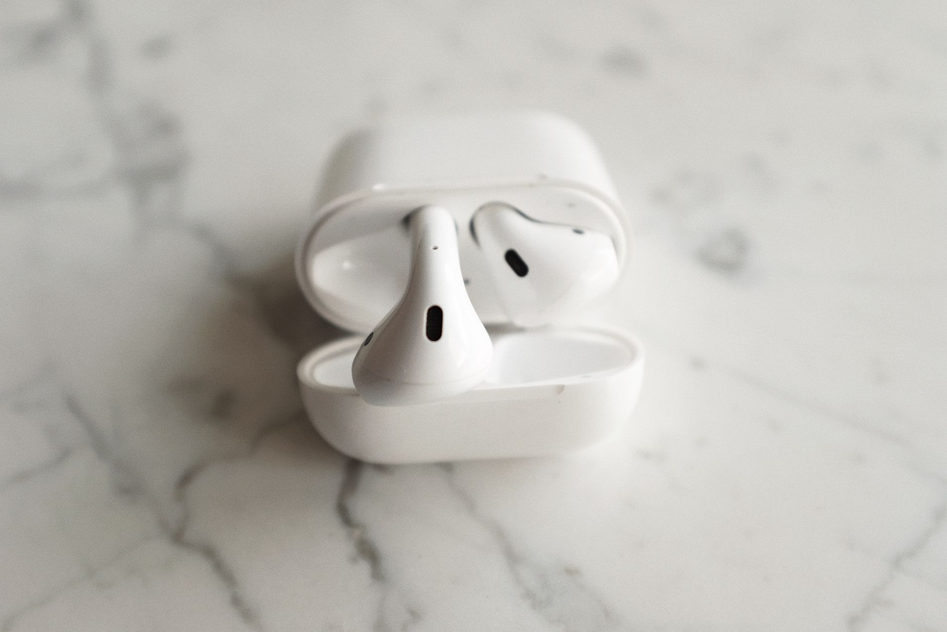 Minimalistic image of wireless earbuds with case open on a sleek marble background.