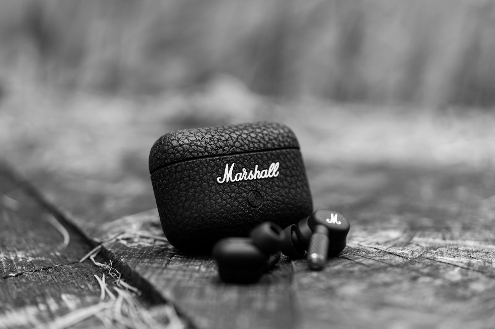 Black Marshall earbuds resting on textured wood. Close-up shot highlighting design and texture.