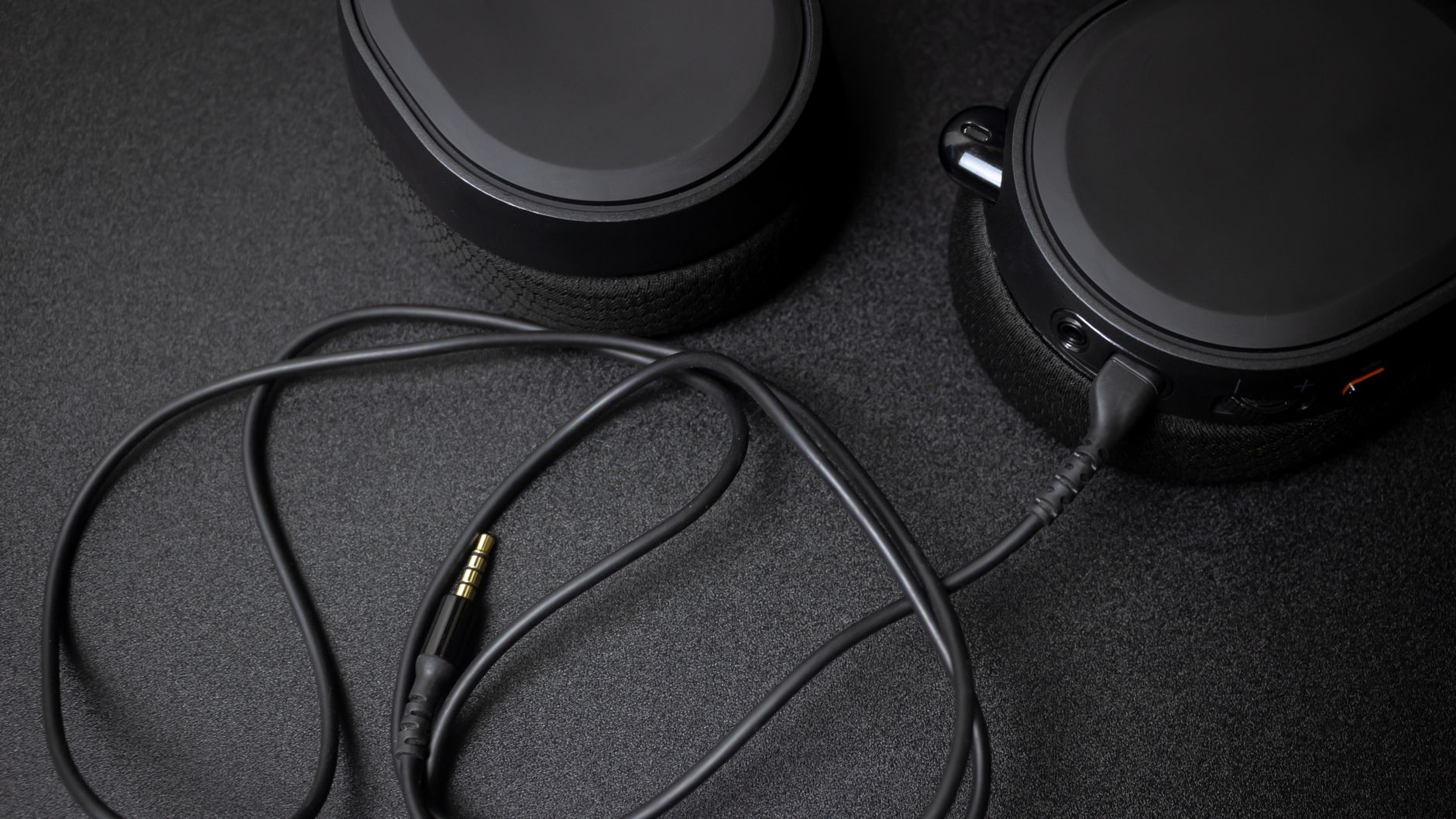 Detailed close-up of a sleek black wired gaming headset with detachable cable on a textured dark surface.