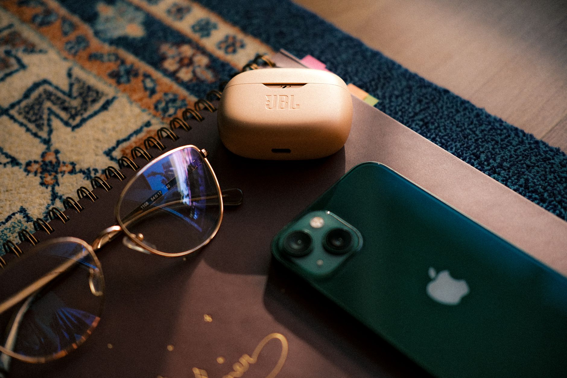 Flat lay of eyewear, smartphone, earbuds, and a notebook on a patterned rug.