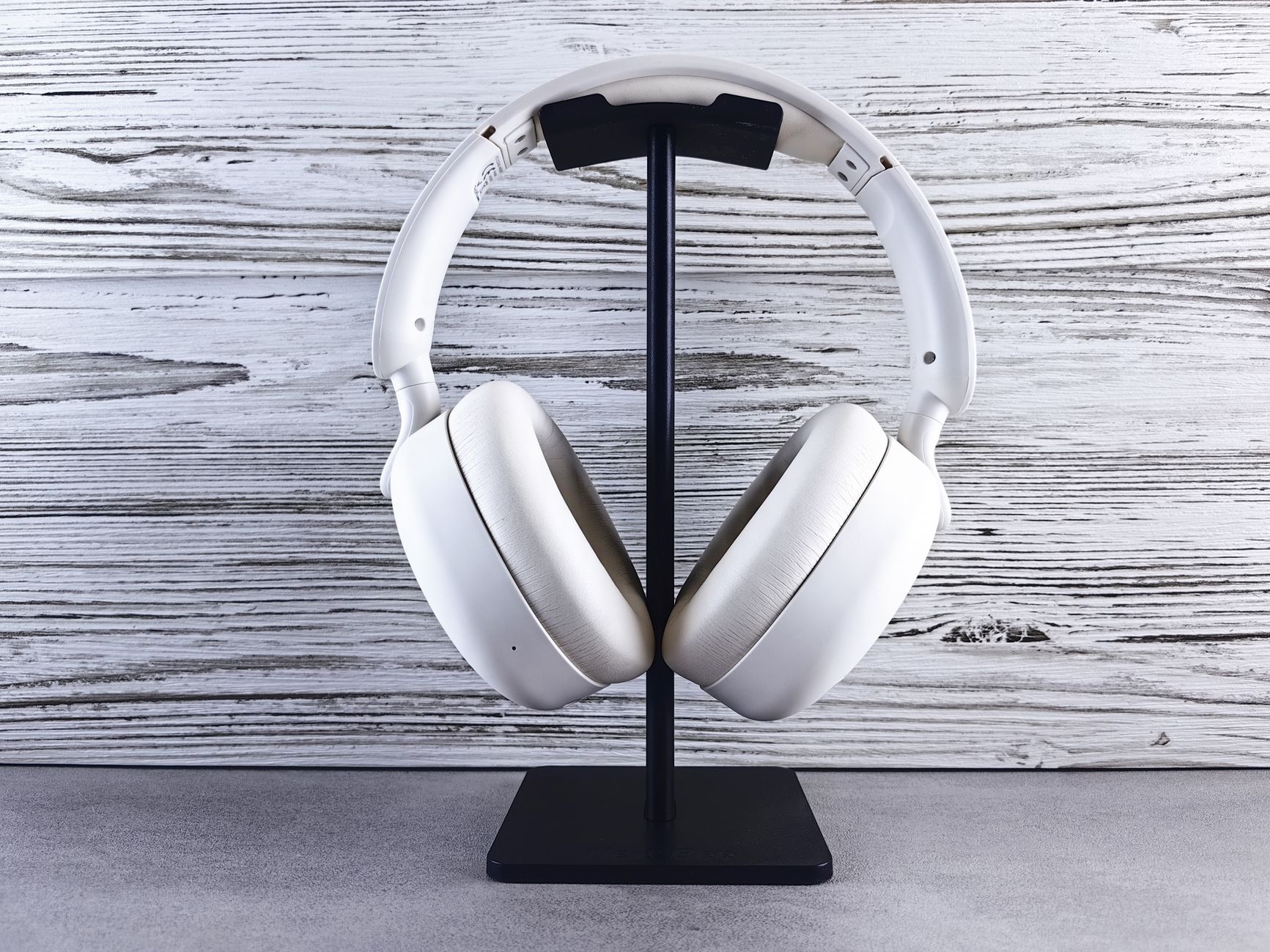 Stylish white wireless headphones displayed on a sleek stand against a wood background.