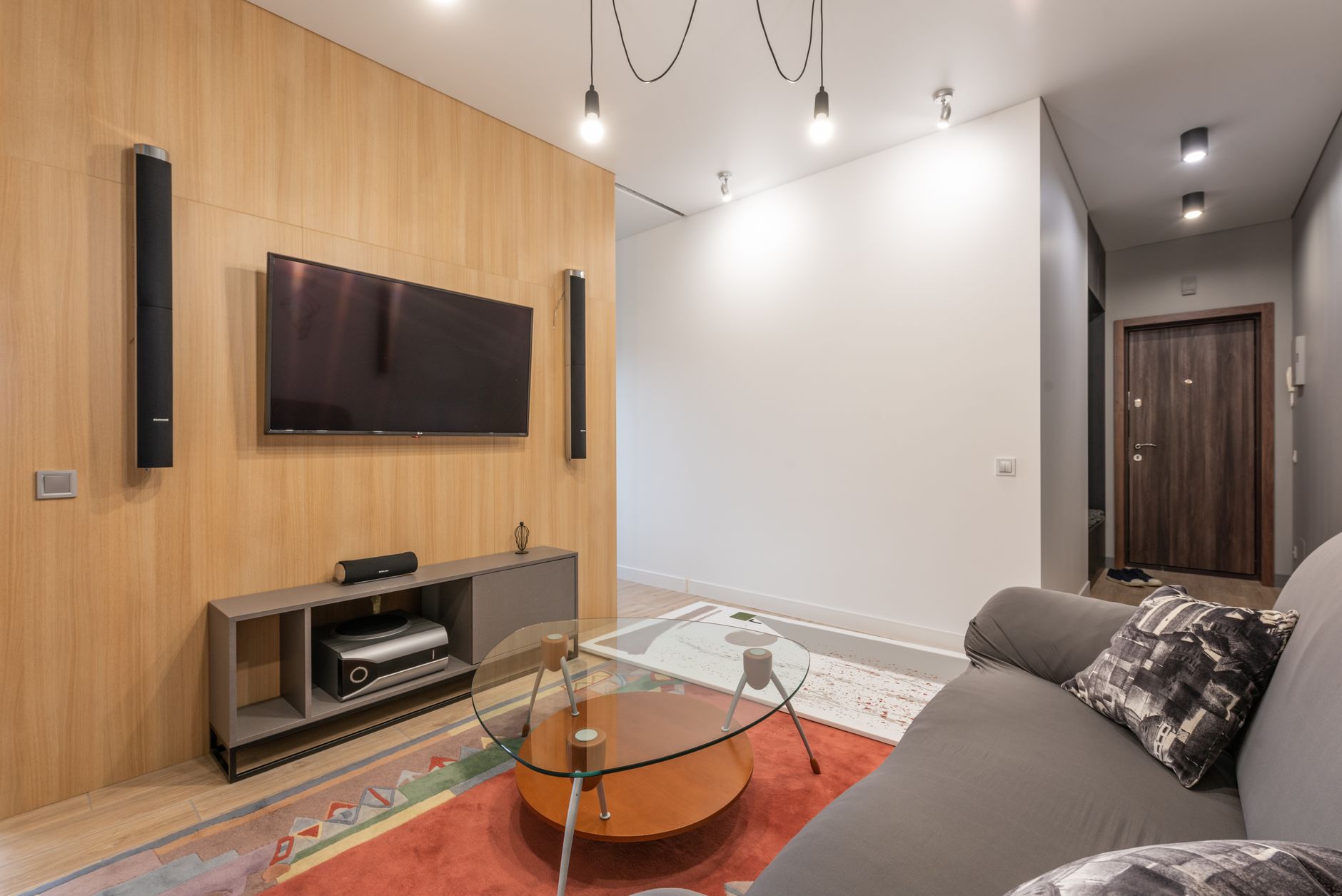 Interior of contemporary light apartment with couch with pillows near table on carpet and cabinet with TV on wall with speakers near lamps o