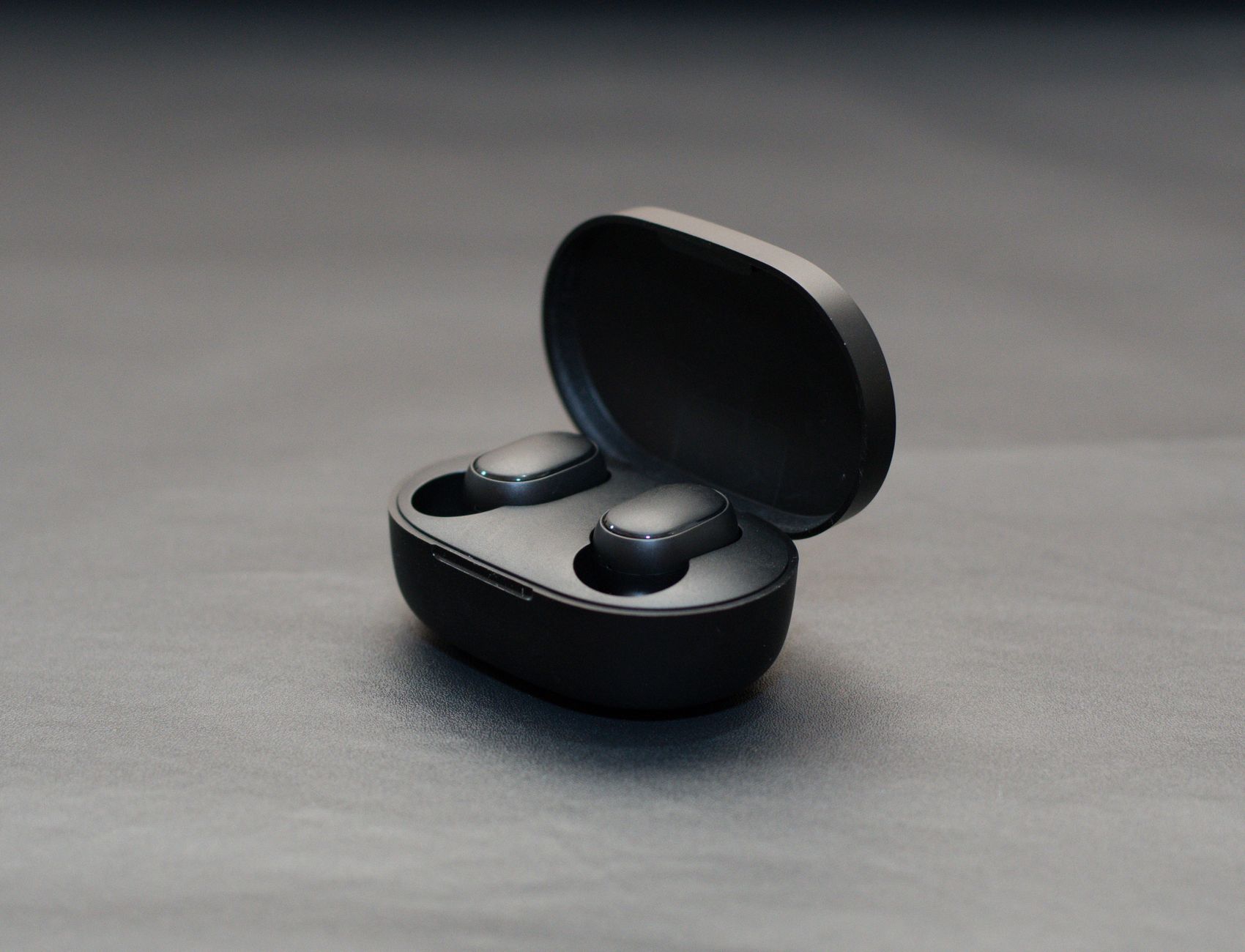 Modern wireless earbuds in an open black charging case on a matte surface.
