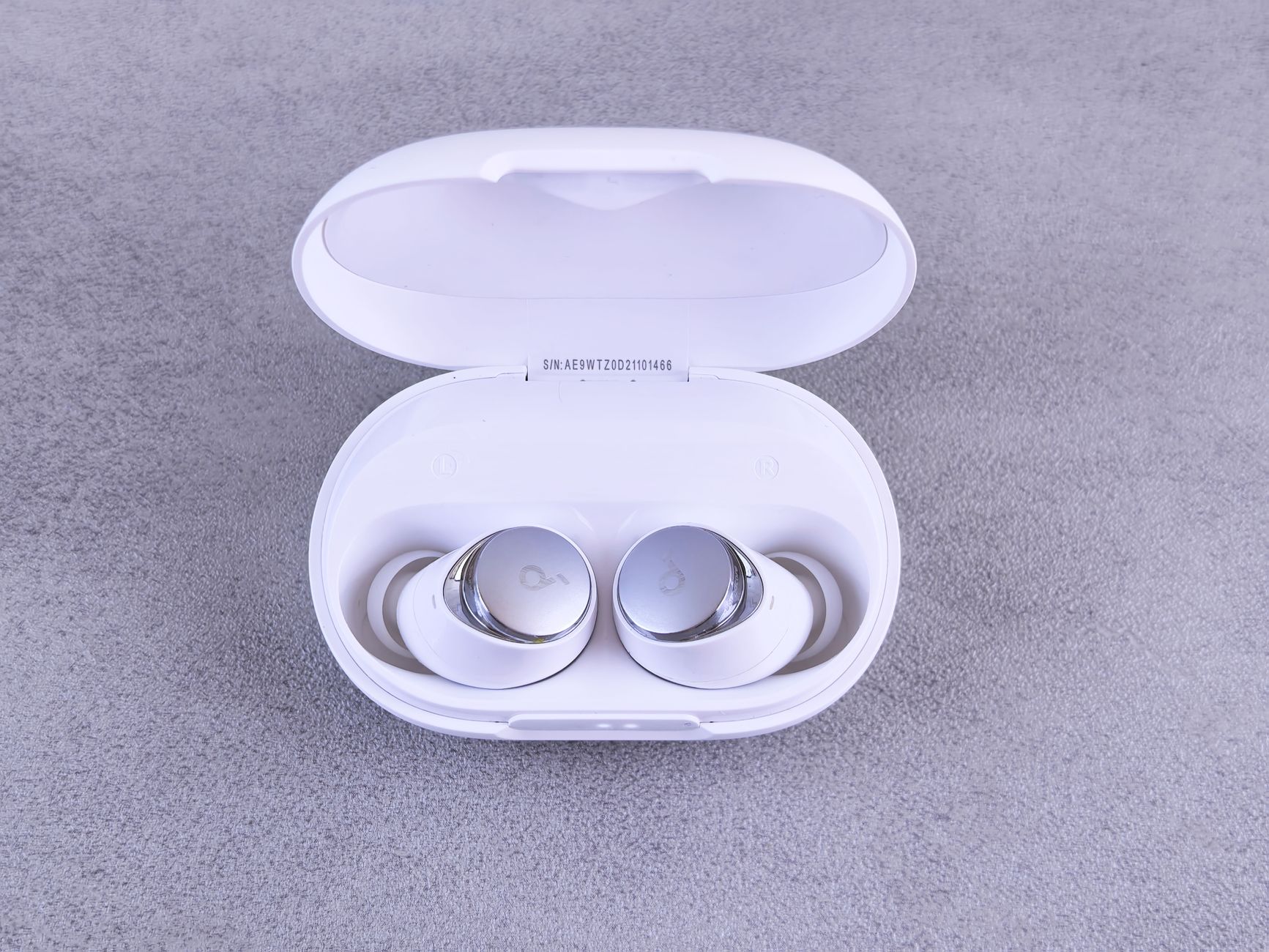 High-quality white wireless earbuds displayed in an open charging case on a textured surface.