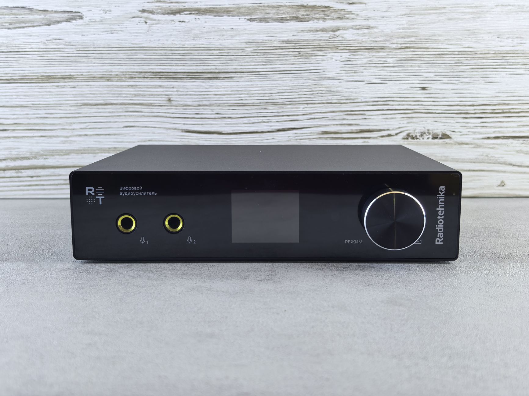 Black audio amplifier with minimalist design and yellow inputs on a wood-patterned backdrop.