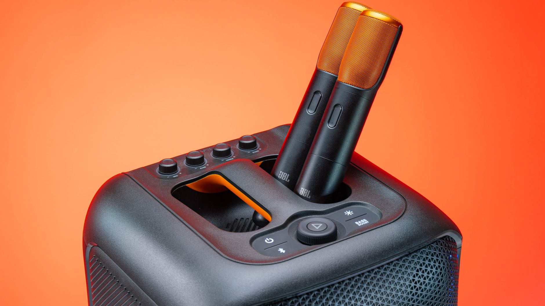 Modern JBL speaker featuring two wireless microphones, set against a vibrant orange background.