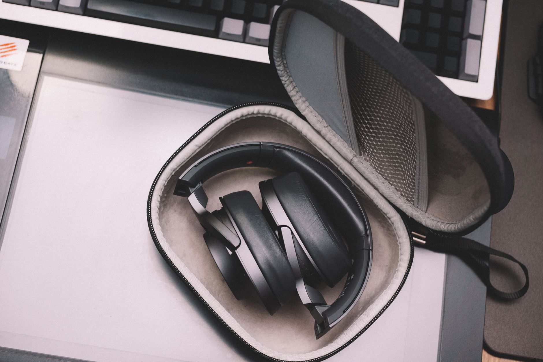 Compact black wireless headphones stored in a protective case placed on a desk, showcasing modern technology.