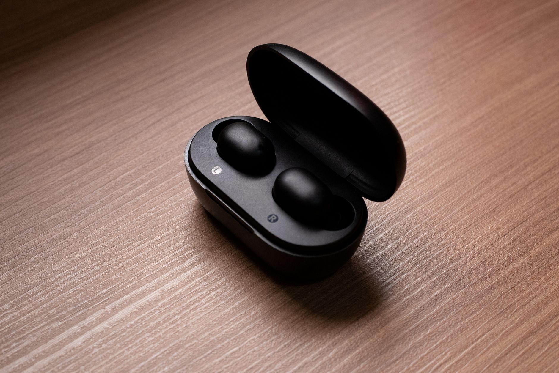 Stylish black wireless earbuds displayed in an open charging case atop a wooden table.
