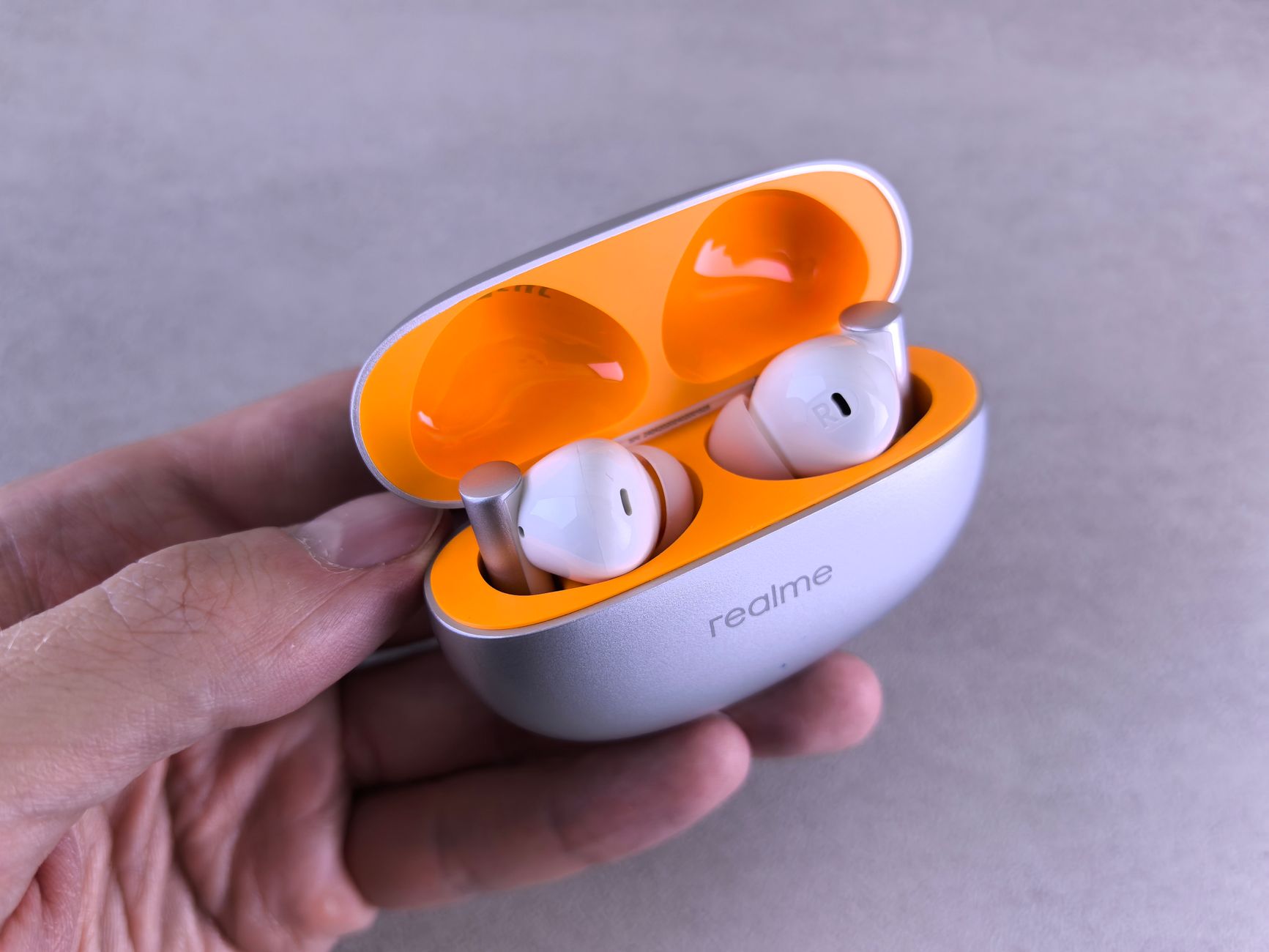 A detailed view of a Realme wireless earbuds set in an open charging case held by a hand.