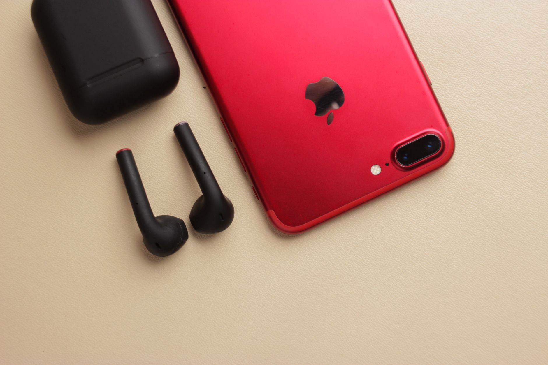 Close-up of a sleek red smartphone with black wireless earbuds and charging case on a beige surface.