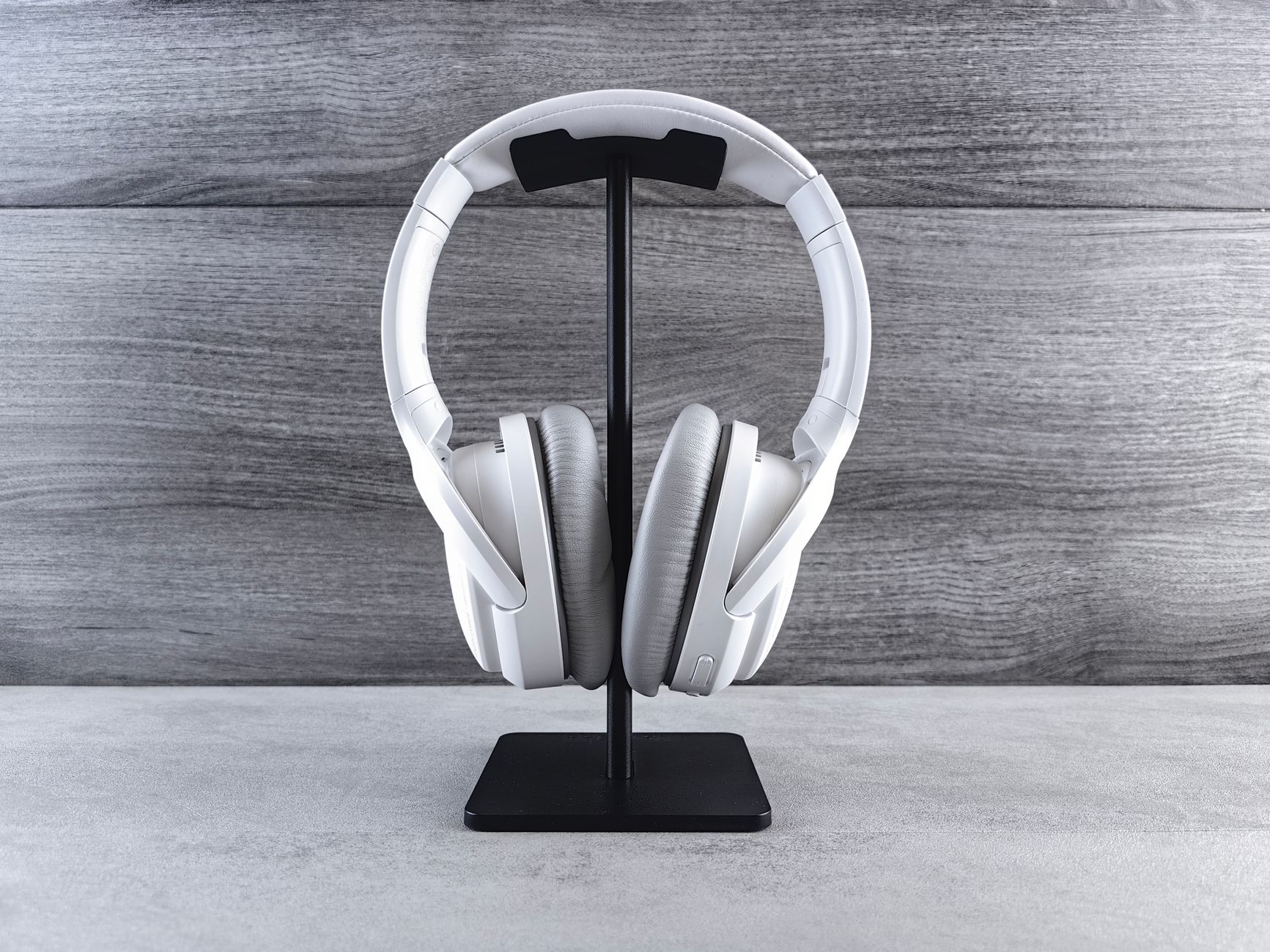 Modern white wireless headphones on a stand against a wooden background, ideal for tech and music themes.