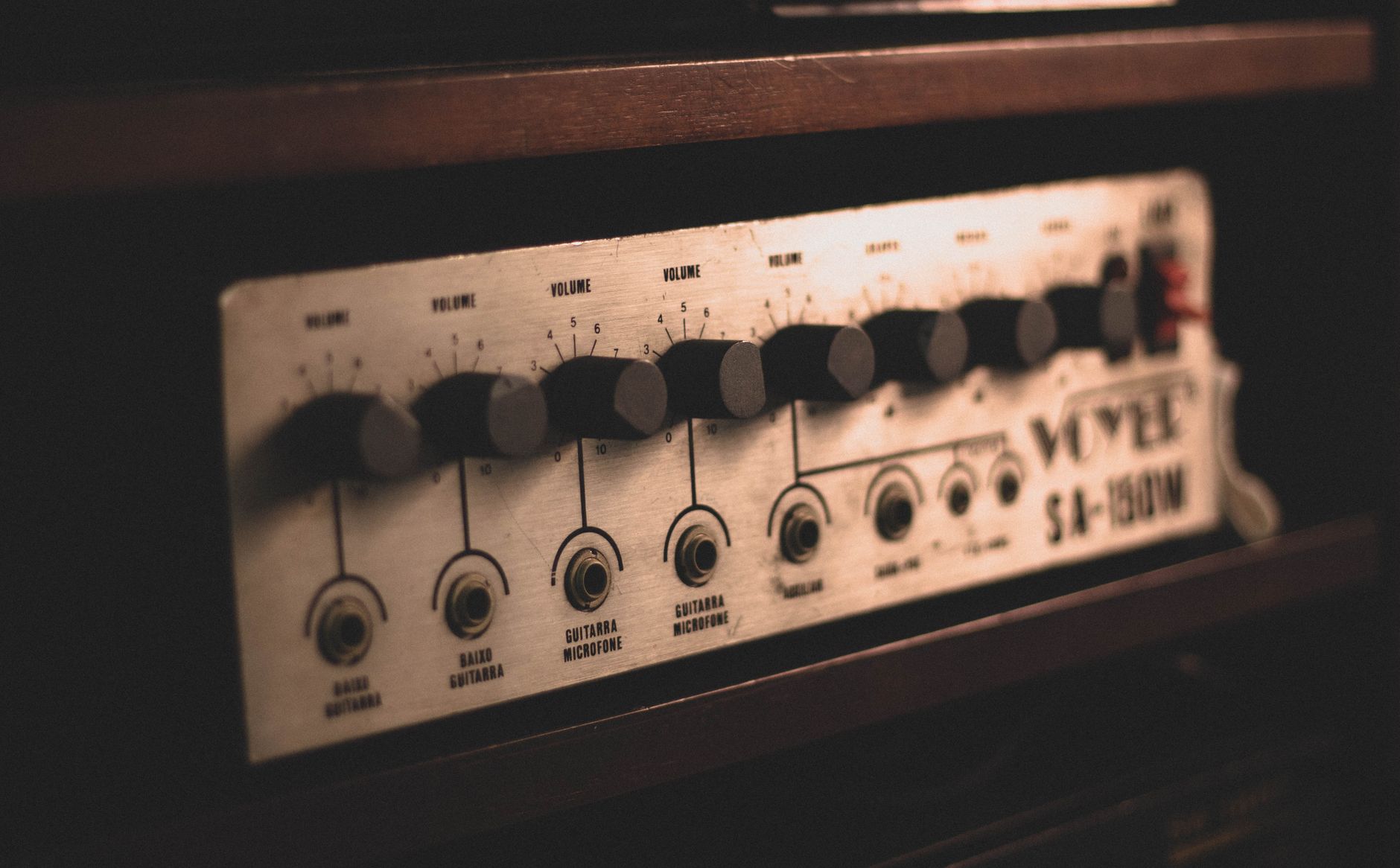 Closeup of professional electronic device amplifier with metal panel and black controllers placed in wooden cabinet