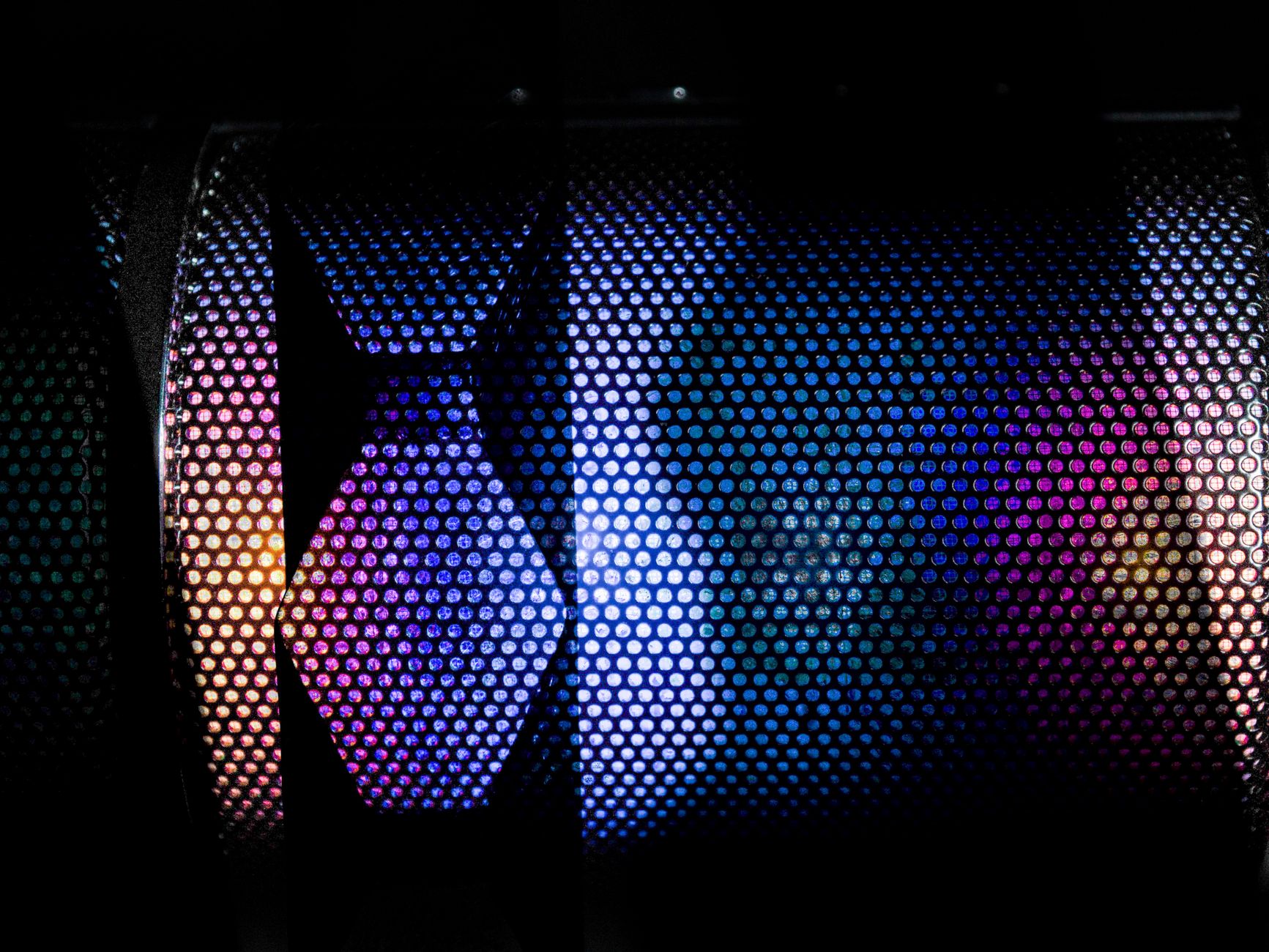 Vibrant close-up of a speaker grille illuminated by colorful lights, showcasing modern technology.