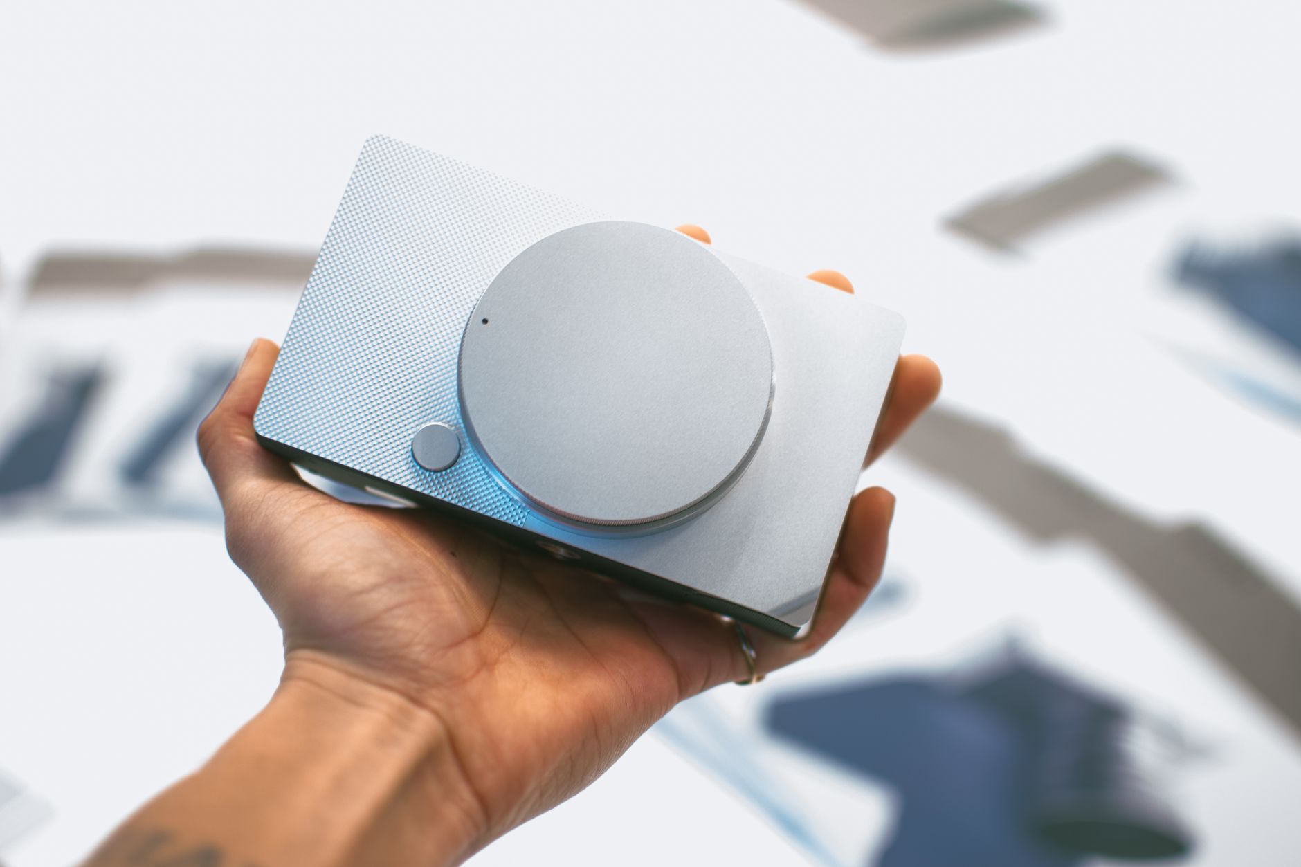 Close-up of a hand holding a sleek gray portable speaker against a blurred background.