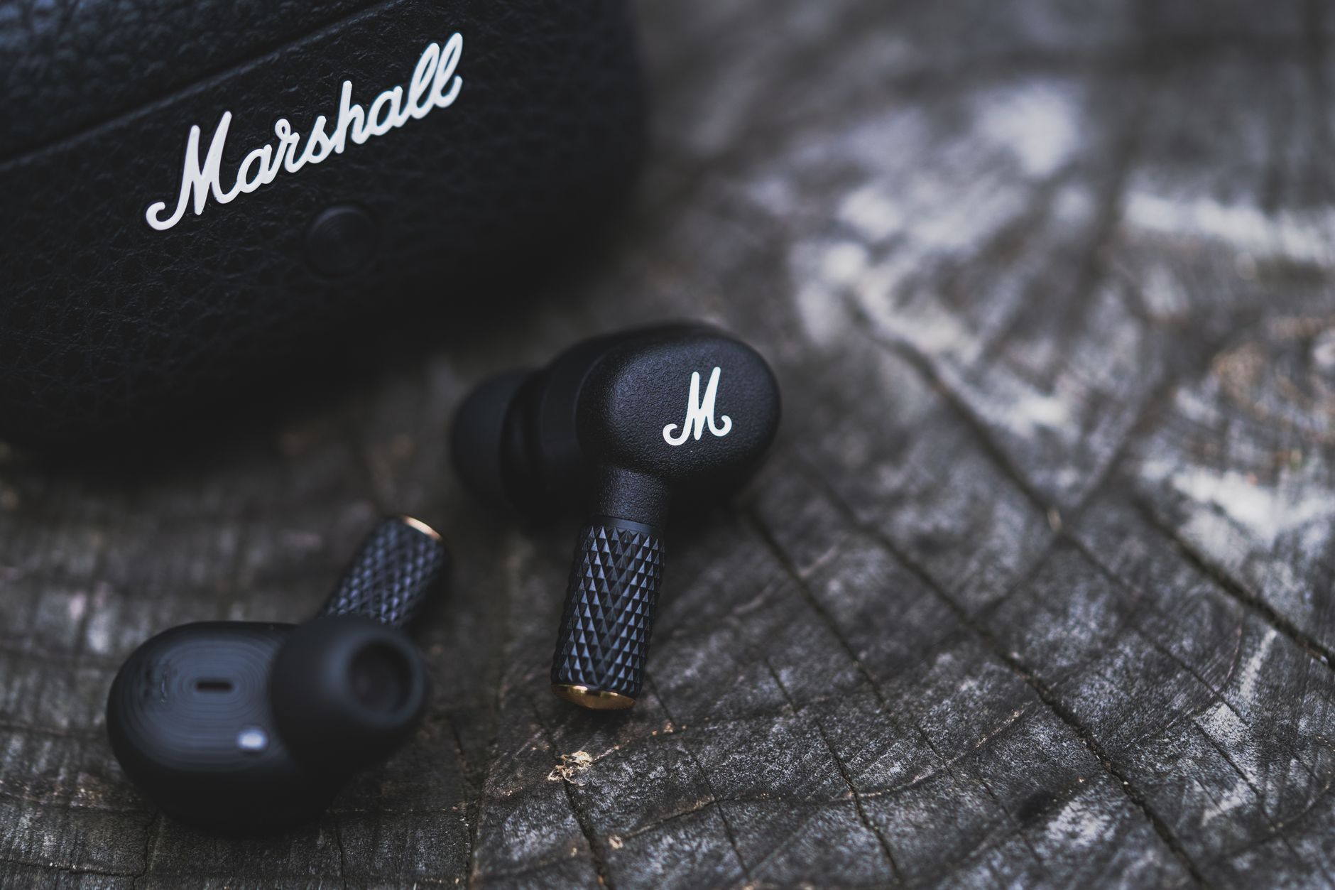 Close-up of black earbuds with textured design resting on a wooden surface, showcasing modern style.