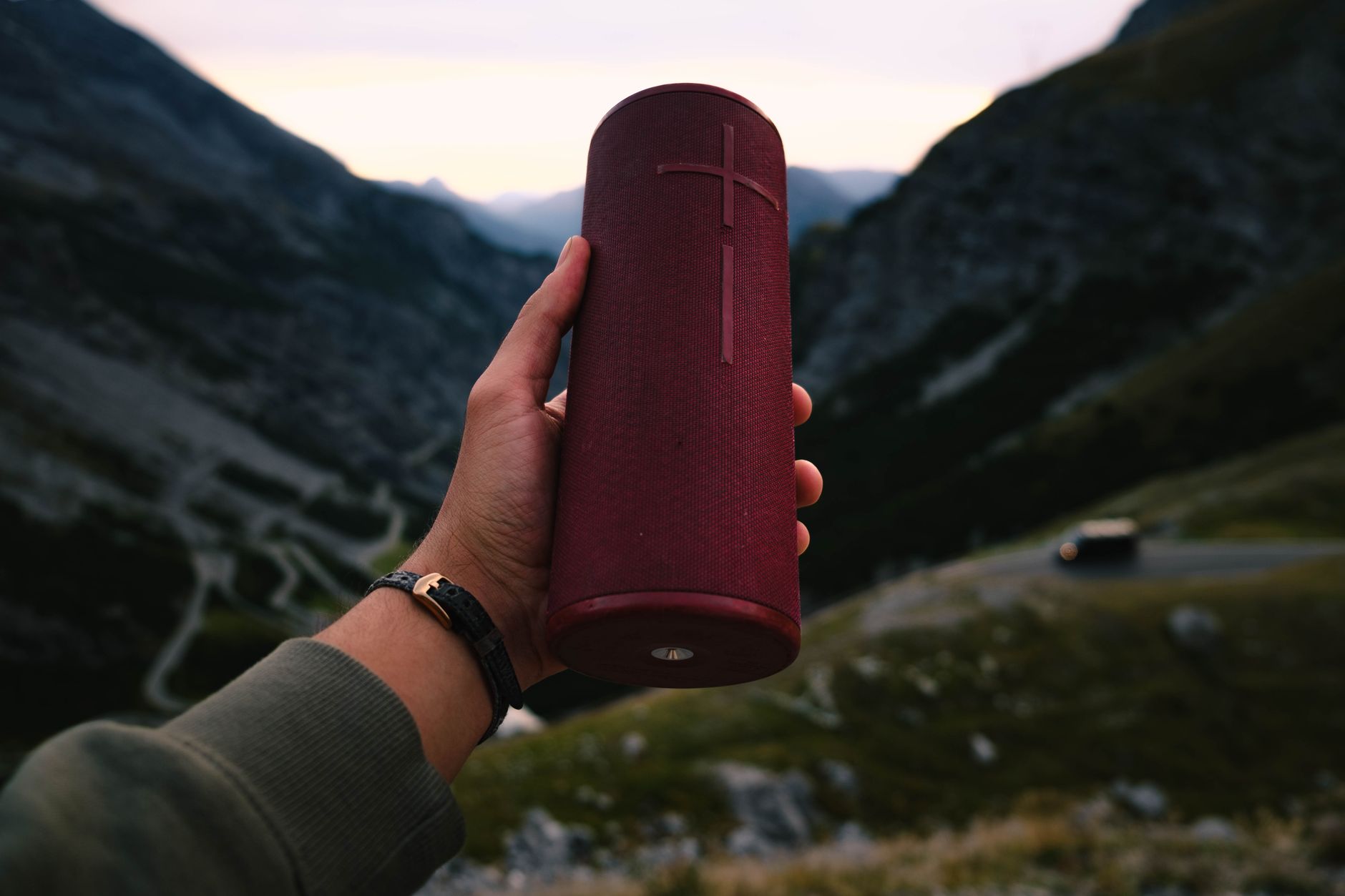 A person holding a red portable speaker with picturesque mountain backdrop.