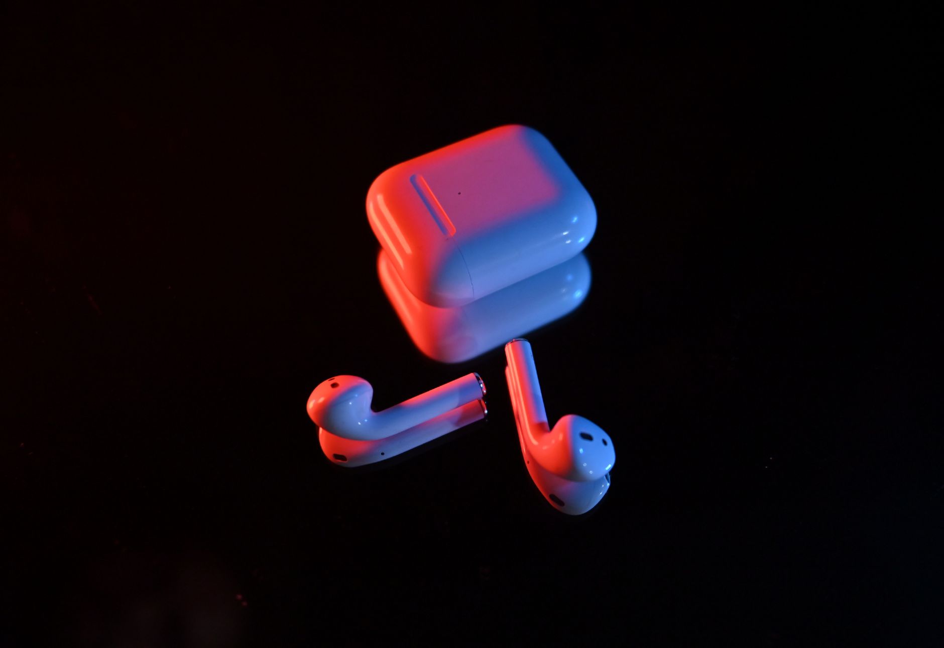 Wireless earbuds and charging case illuminated by red and blue lights on a dark background.