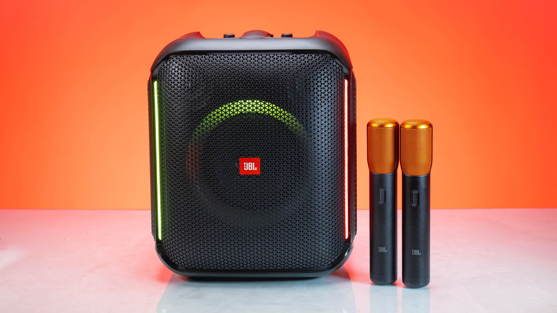 A wireless speaker with two microphones, set against a vivid orange background for a studio shoot.