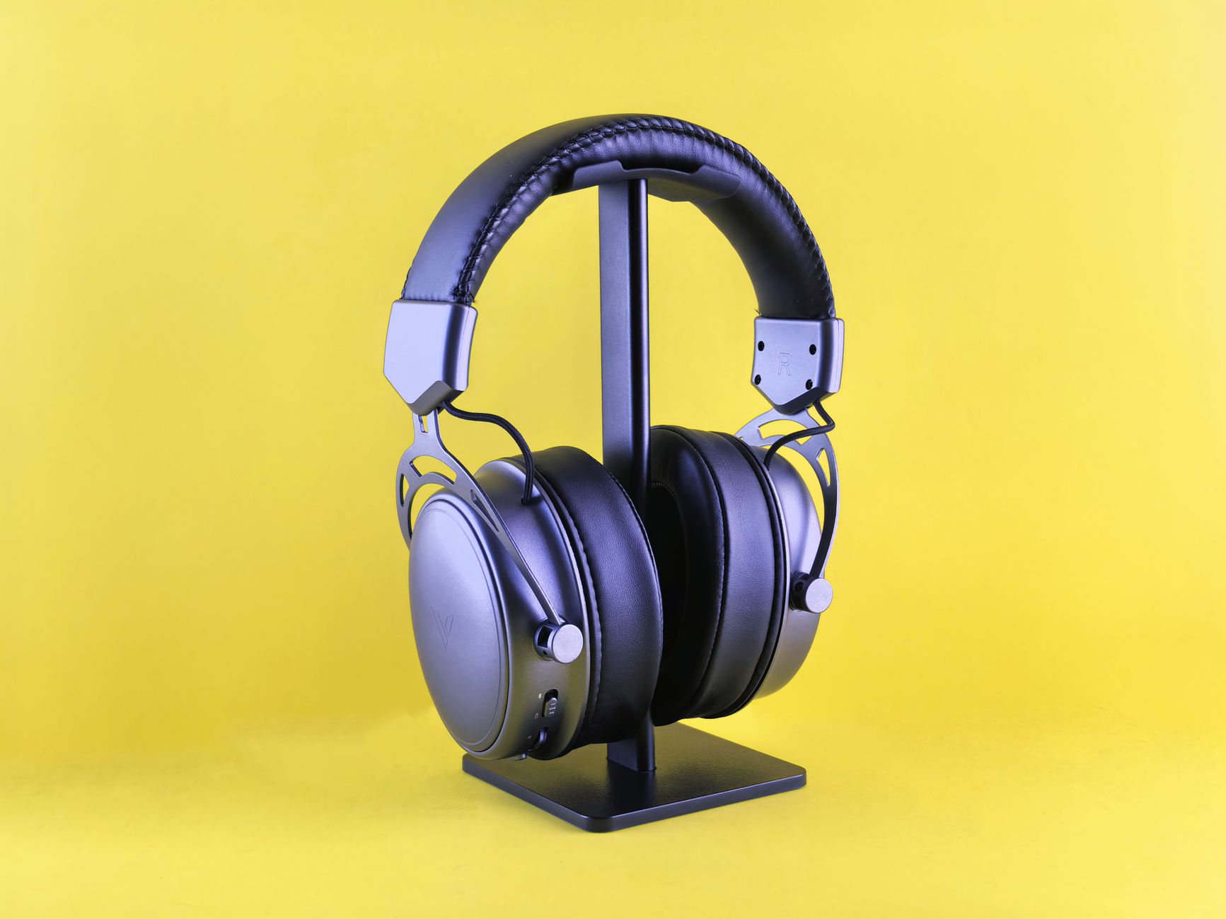 Sleek black headphones on a stand against a vivid yellow backdrop, highlighting modern audio design.