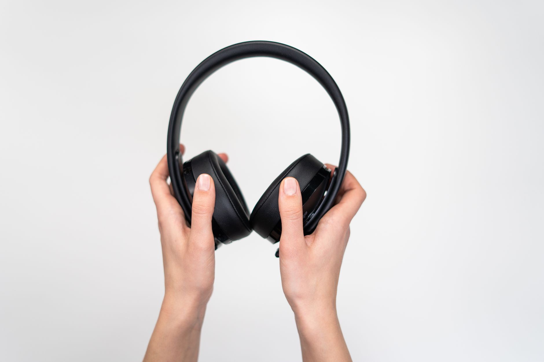 Close-up of hands holding black over-ear headphones on a white background.