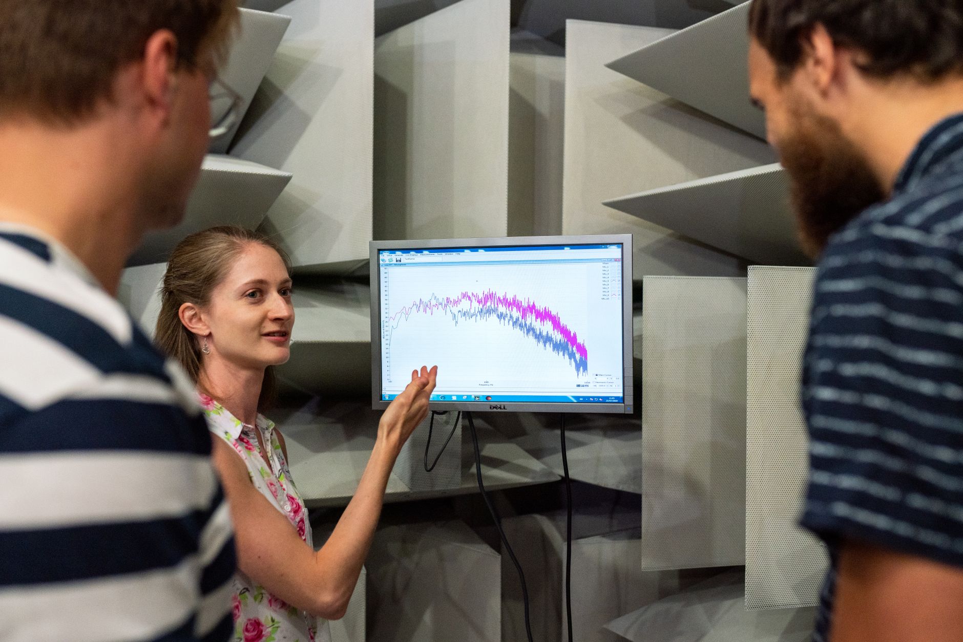 Three engineers discussing sound waves displayed on a monitor in a professional sound studio.