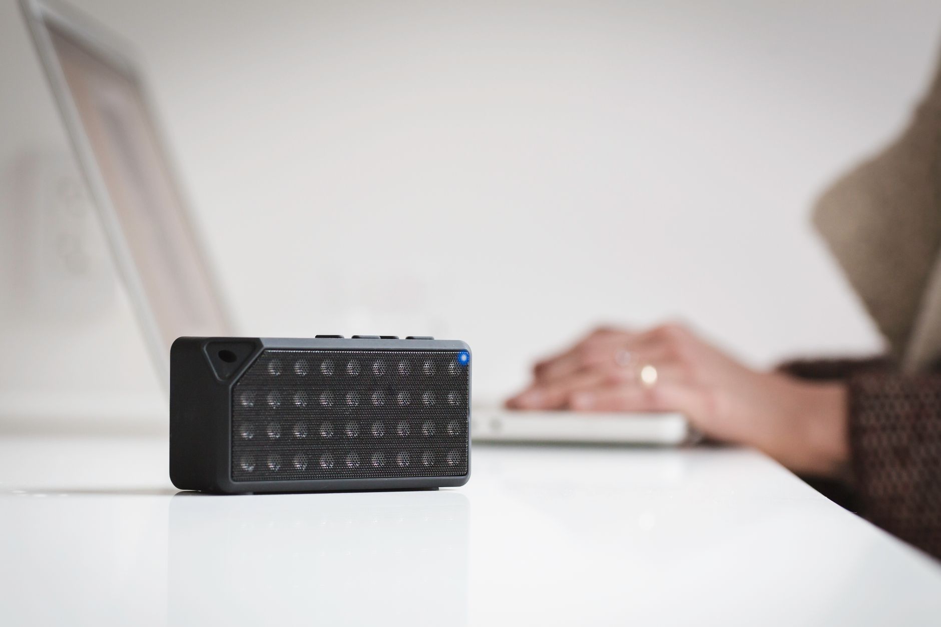 A sleek wireless speaker on a white desk near a laptop, showcasing modern office technology.