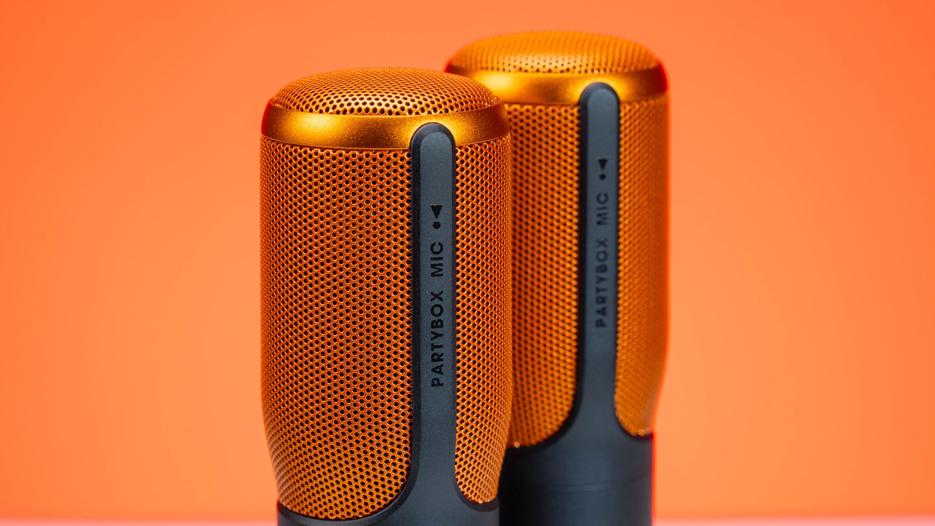 Close-up of two vibrant orange JBL Partybox microphones against an orange backdrop, showcasing modern audio technology.