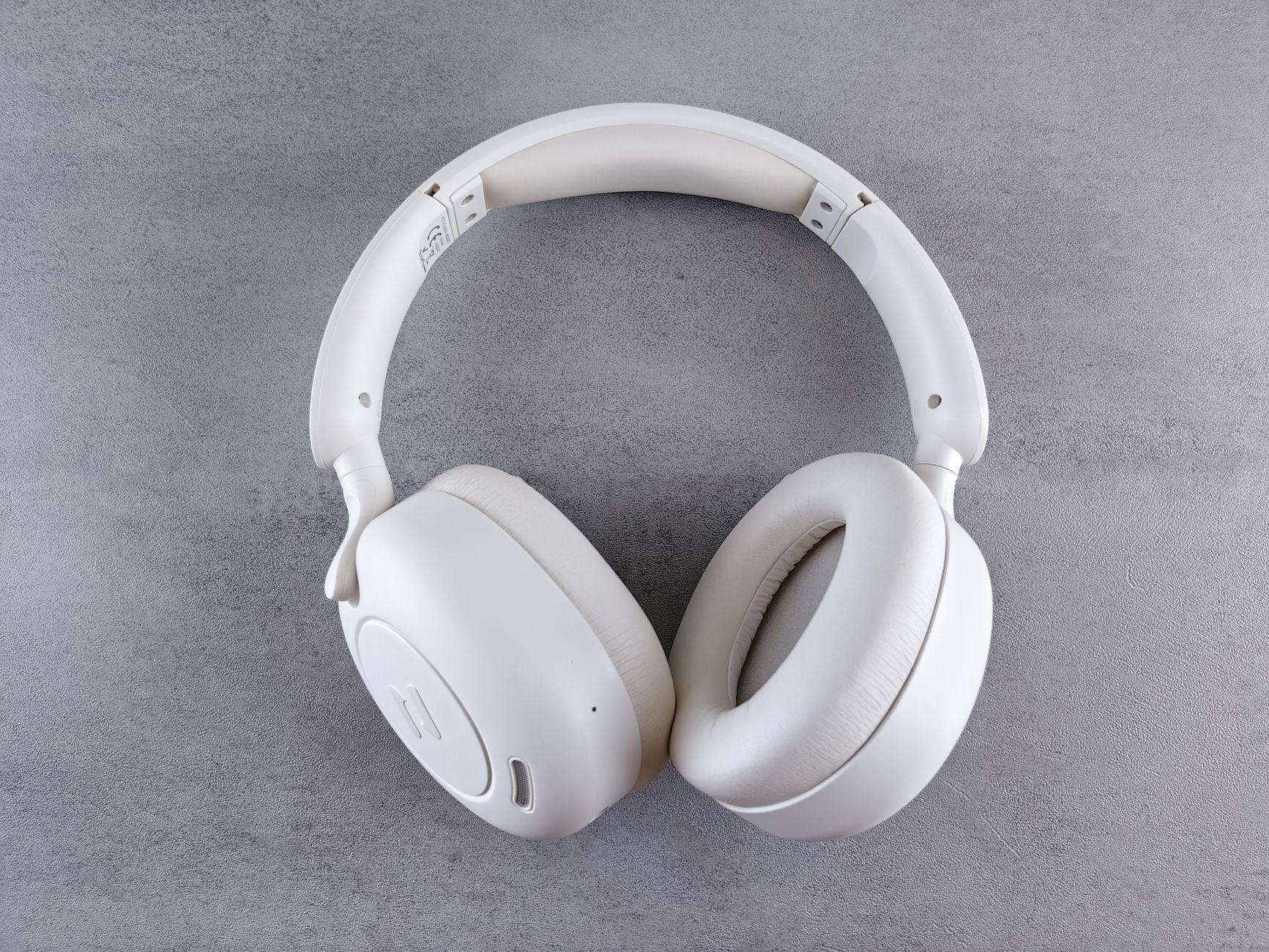 Close-up of sleek white wireless headphones on a textured gray surface. Ideal for audio enthusiasts.