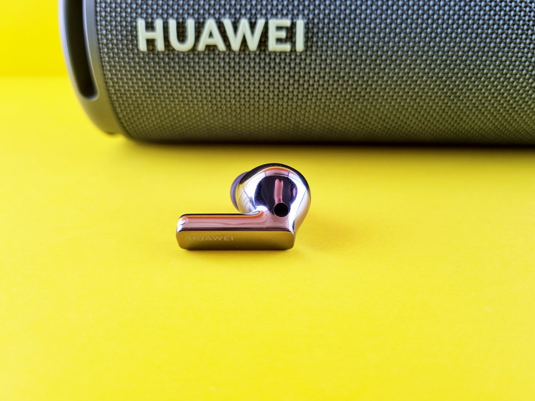 Close-up of a Huawei wireless earbud with a speaker on a vibrant yellow surface for tech and audio representation.