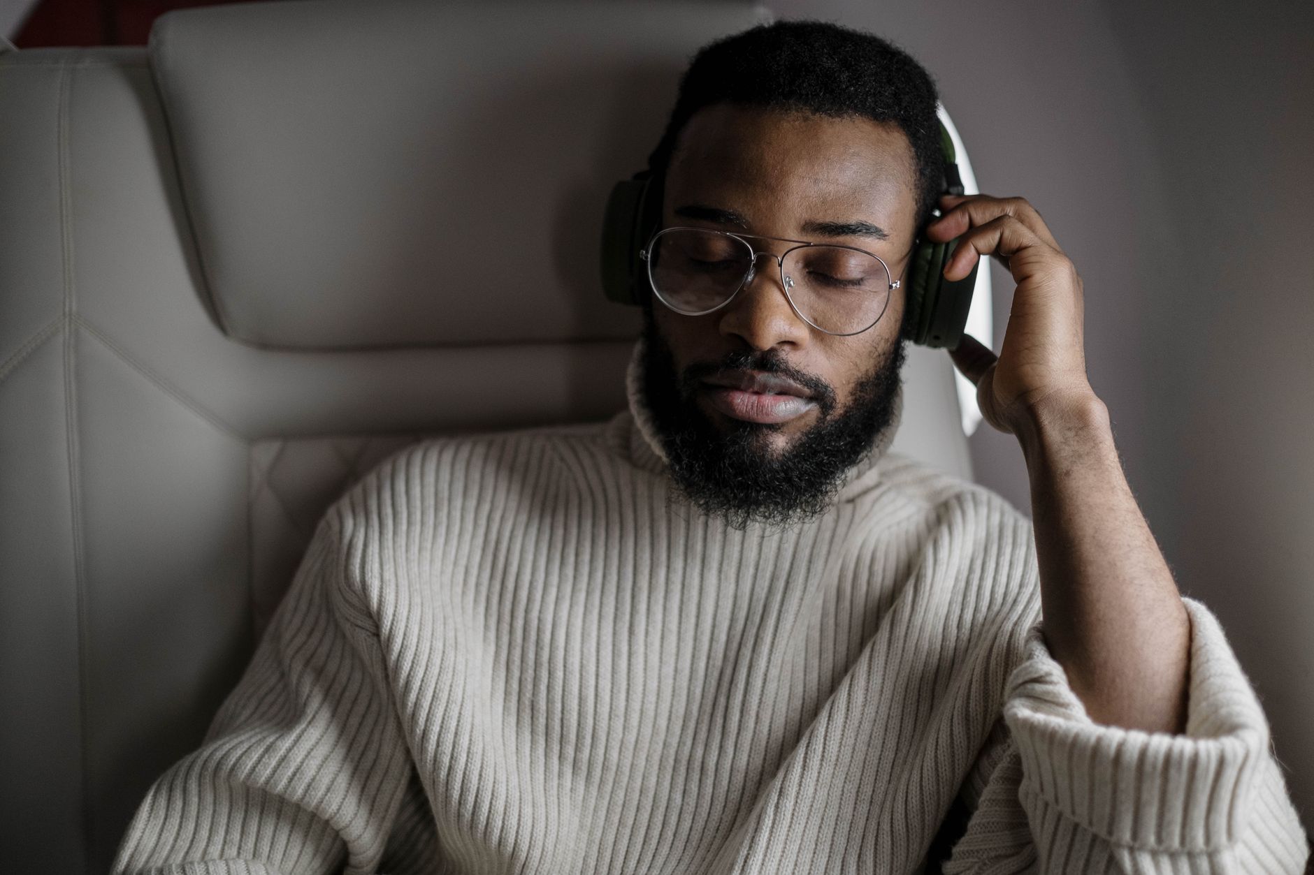 A man in a sweater enjoys music with headphones while sitting on an airplane.