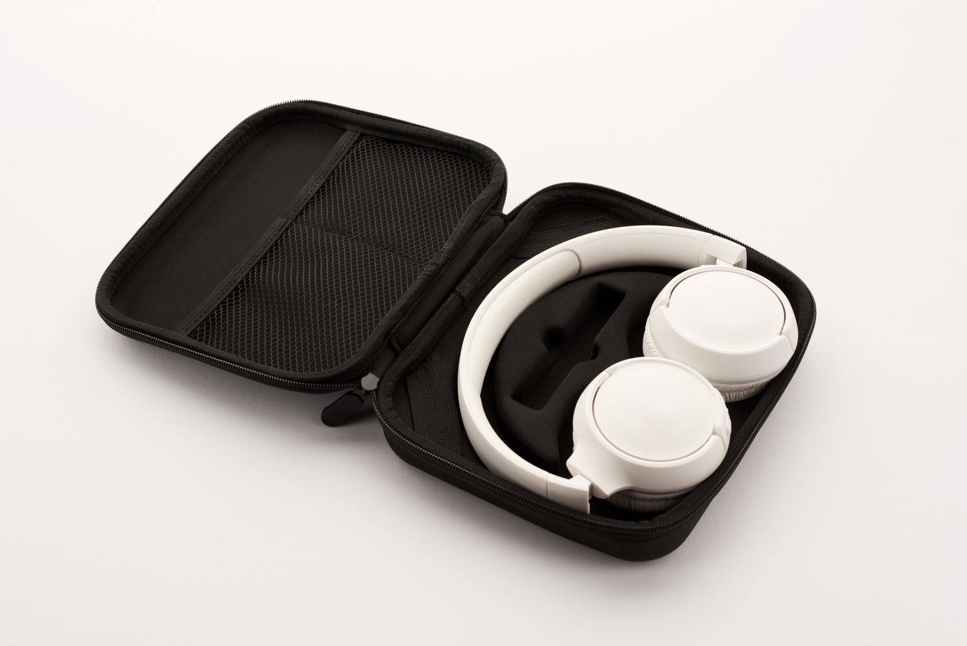 White wireless headphones neatly packed in a black portable travel case on a neutral background.
