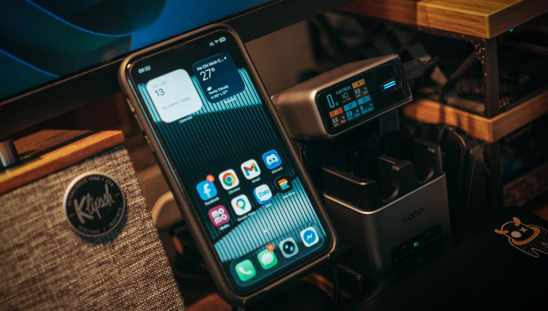 Smartphone and digital charging station on a desk with Klipsch speaker visible.