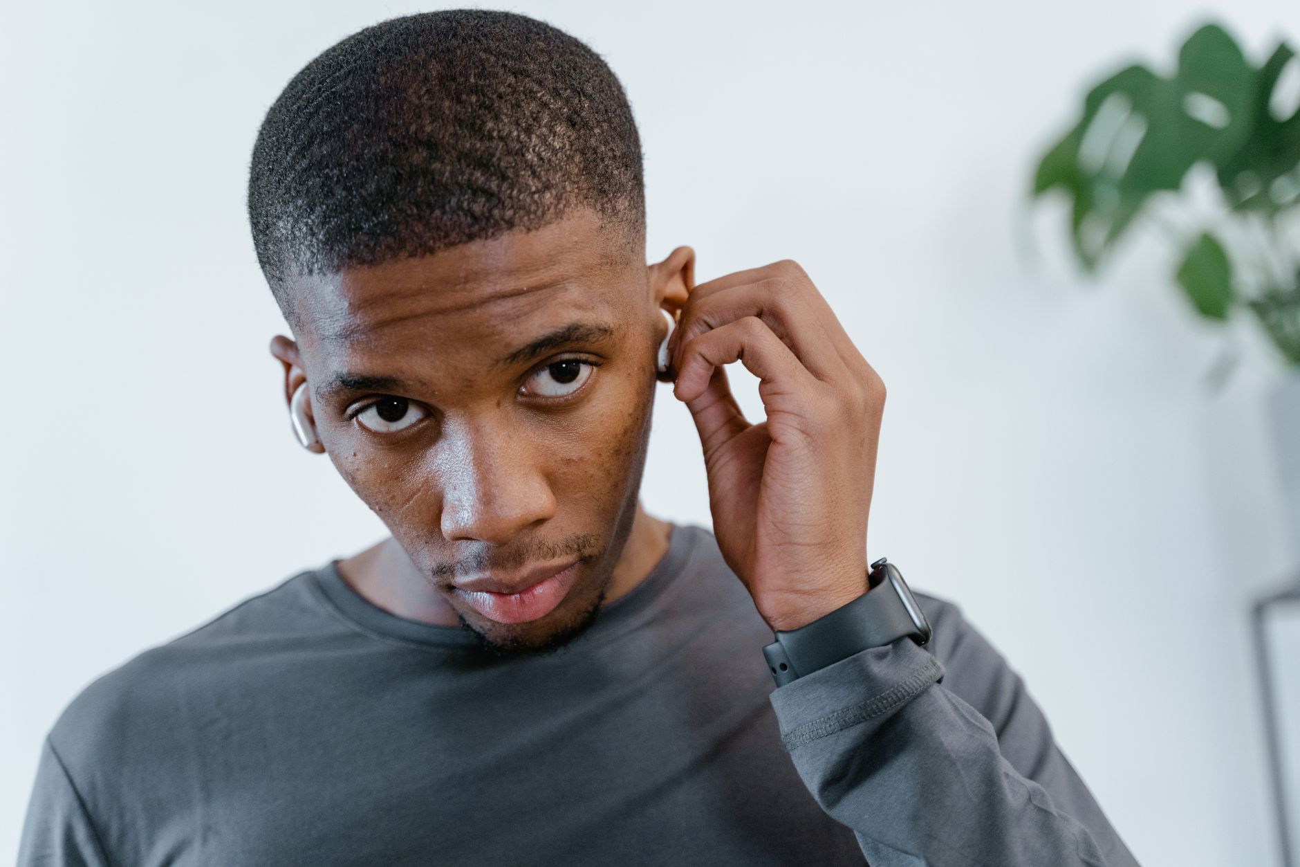 African American man adjusting wireless earphones while wearing casual attire indoors.