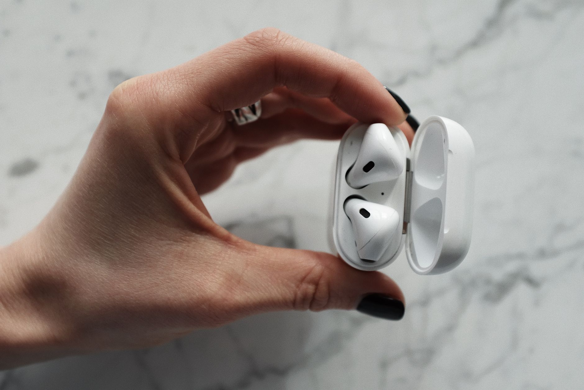 Detailed close-up of a hand holding wireless earbuds in a sleek case against a marble background.