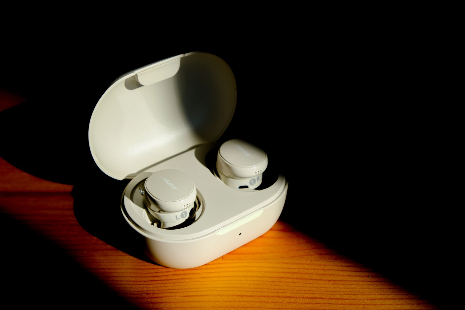 A pair of white wireless earbuds in an open charging case, illuminated against a dark background.