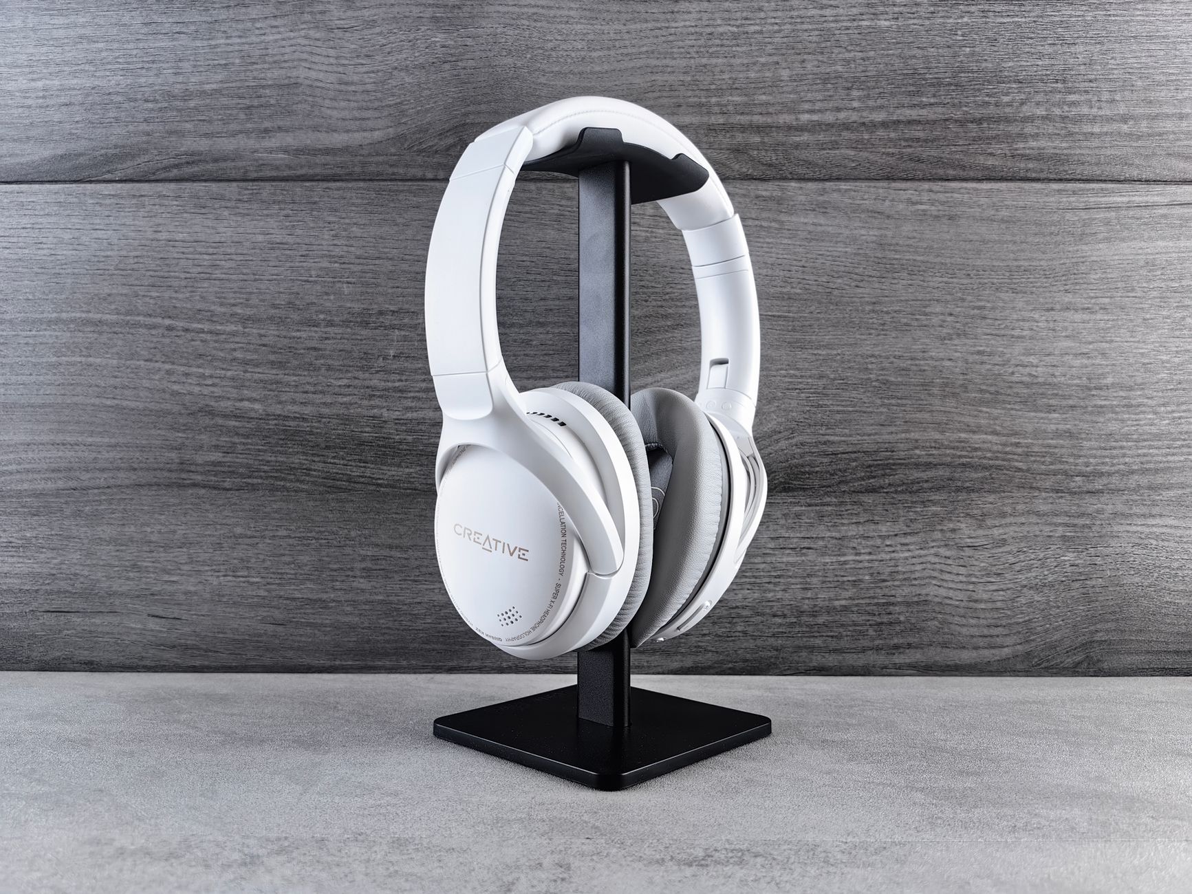 White headphones on a stand against a wooden background, showcasing modern audio equipment.